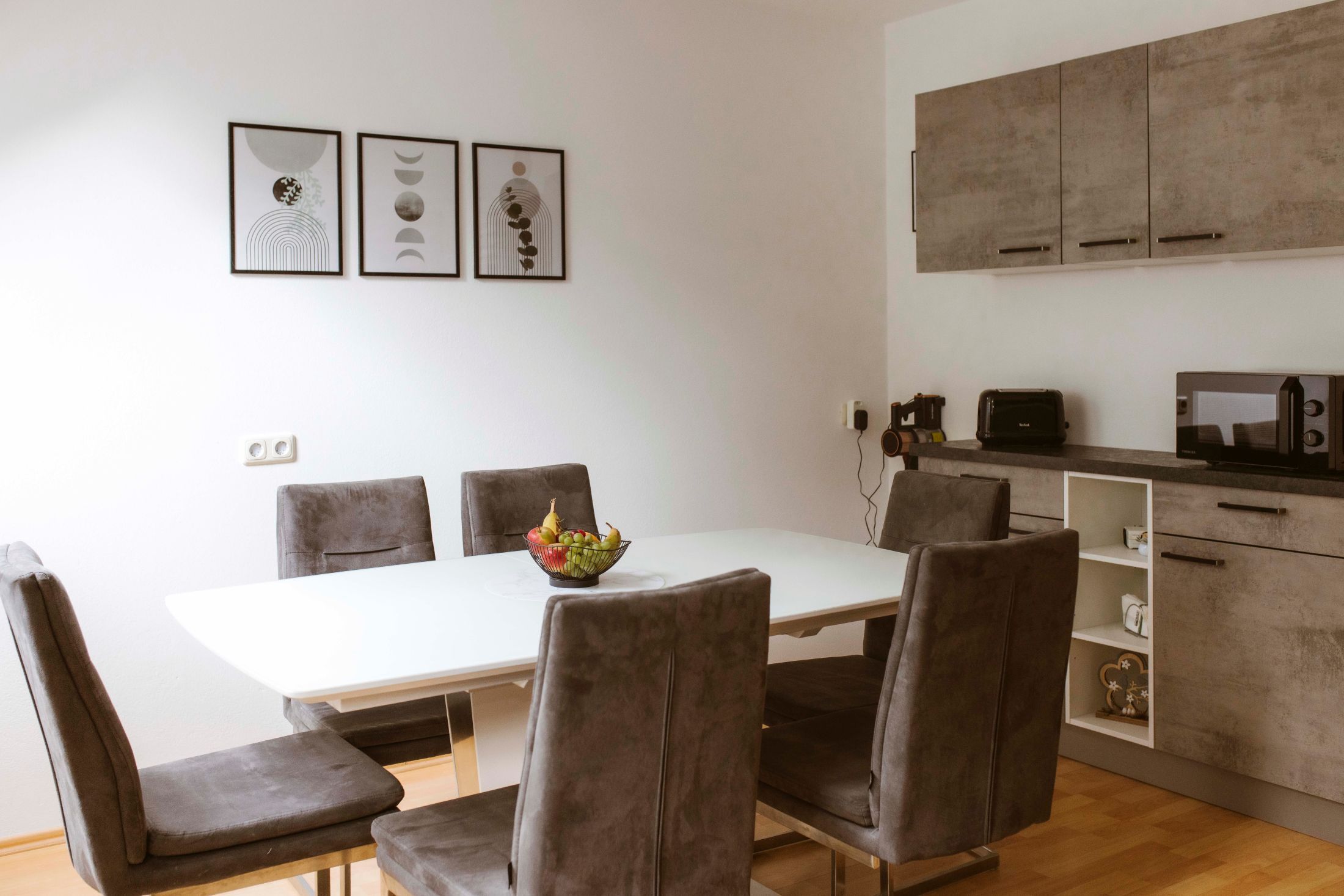 Modern étkező szürke székekkel, fehér asztallal és minimalista dekorációval.