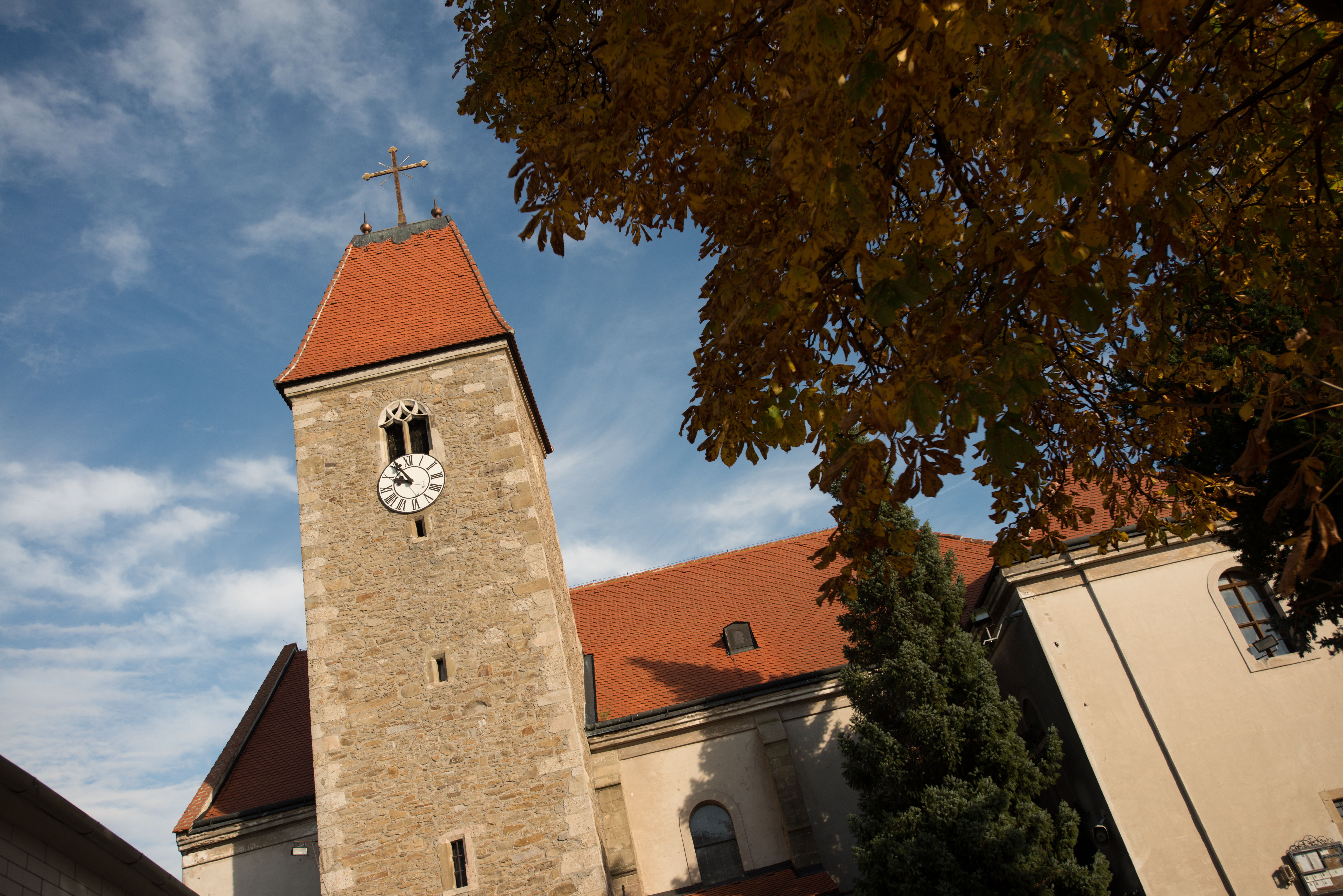 Weißenkirchen templom tornya órával és vörös tetővel, őszi levelekkel és kék éggel körülvéve.