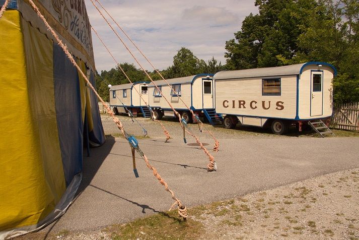 Cirkuszi kocsi és sátor egy kavicsos területen.