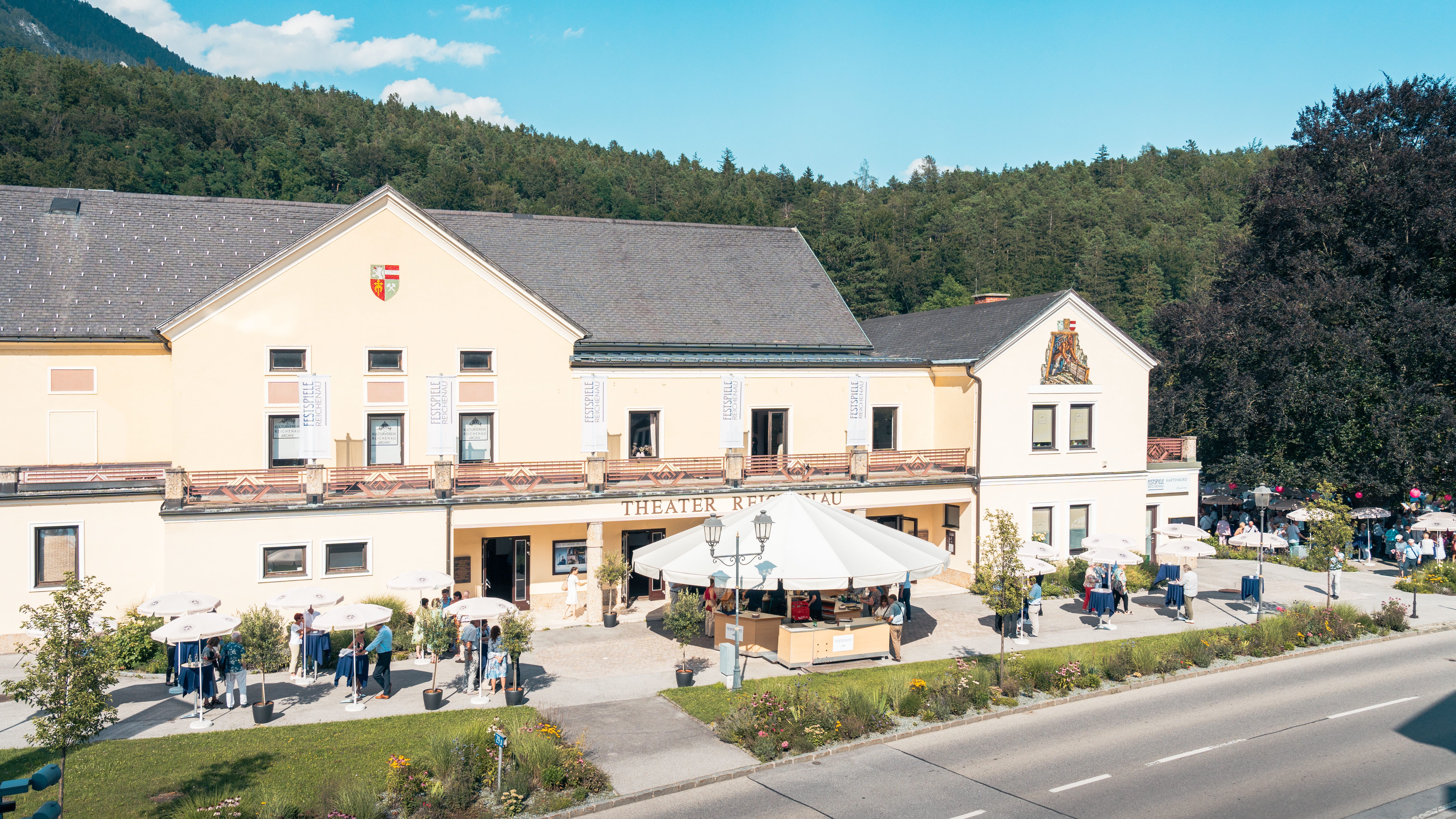 Reichenau Színház, előtte emberek és napernyők.