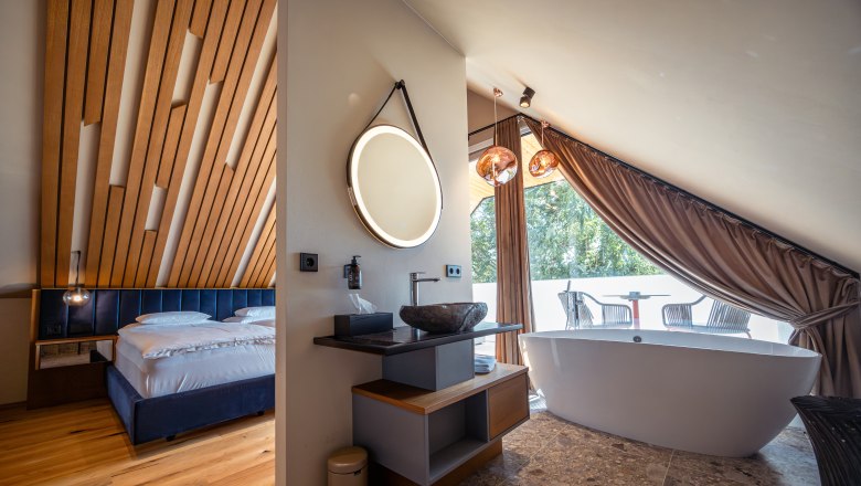 Modern szállodai szoba fából készült mennyezettel, szabadon álló káddal és erkéllyel.