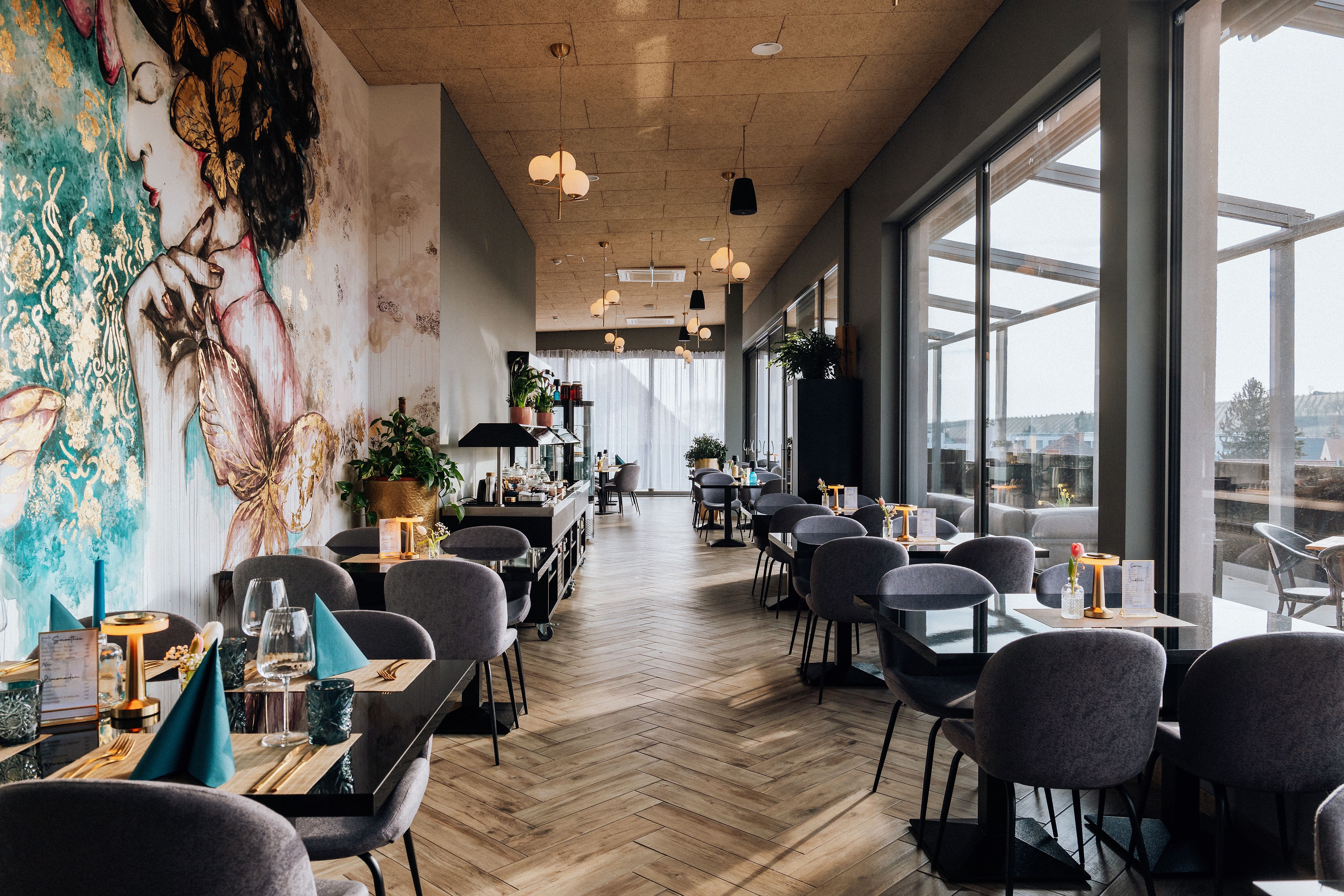 Egy elegáns étterem belső nézete, nagy ablakokkal és művészi falfestményekkel.