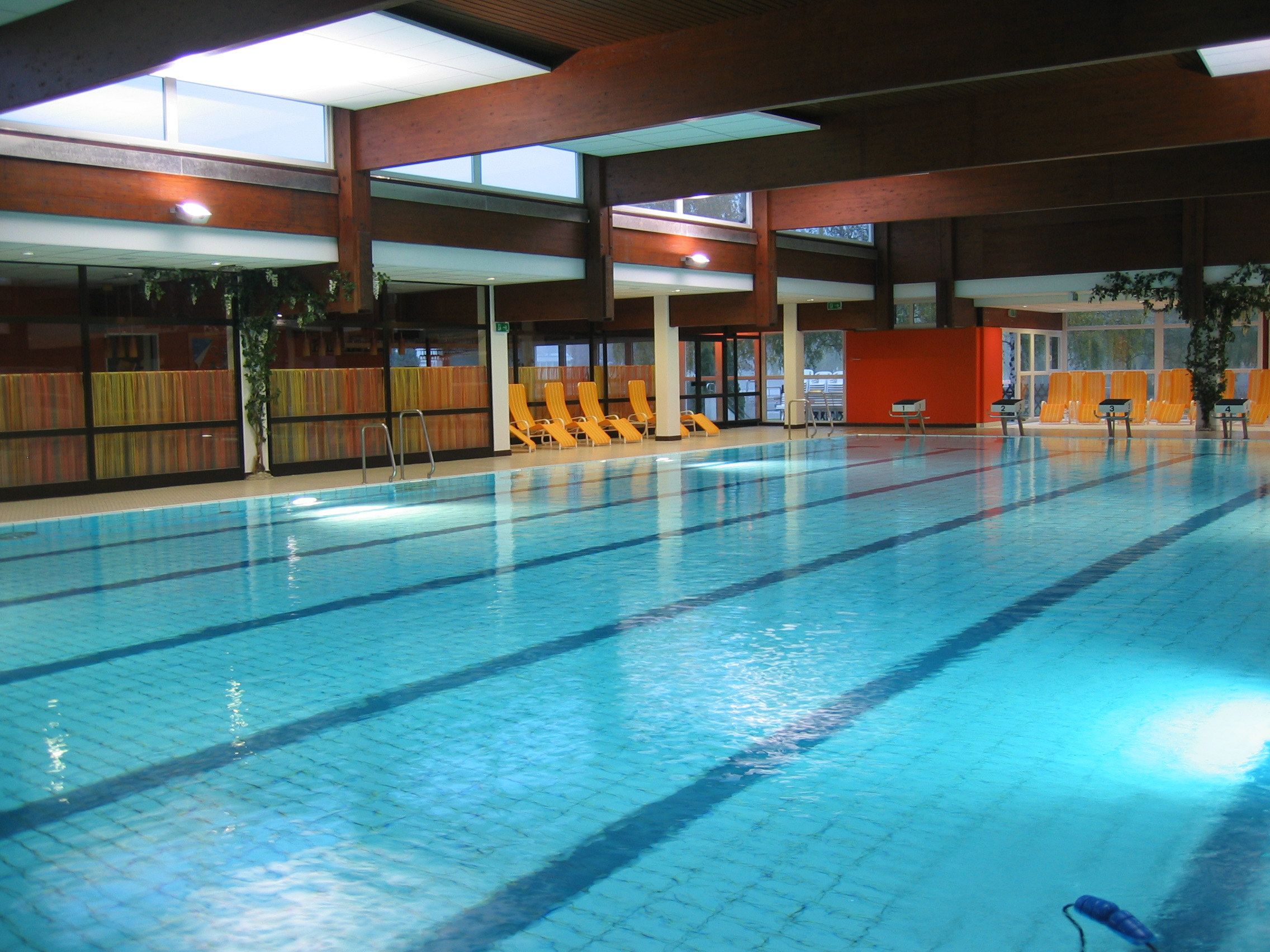 Belső nézet egy úszómedencéről, üres nyugágyakkal a medence szélén.