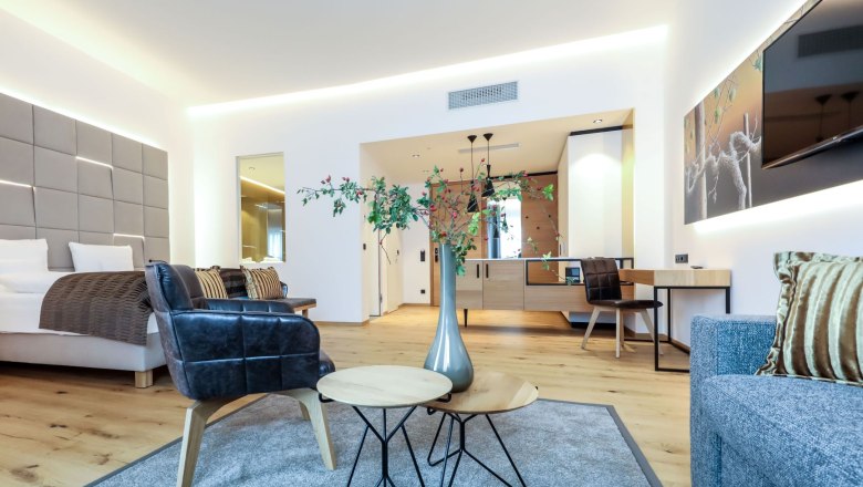 Modern&uuml;l berendezett sz&aacute;llodai szoba &aacute;ggyal, fotelekkel, asztallal &eacute;s dekor&aacute;ci&oacute;val.