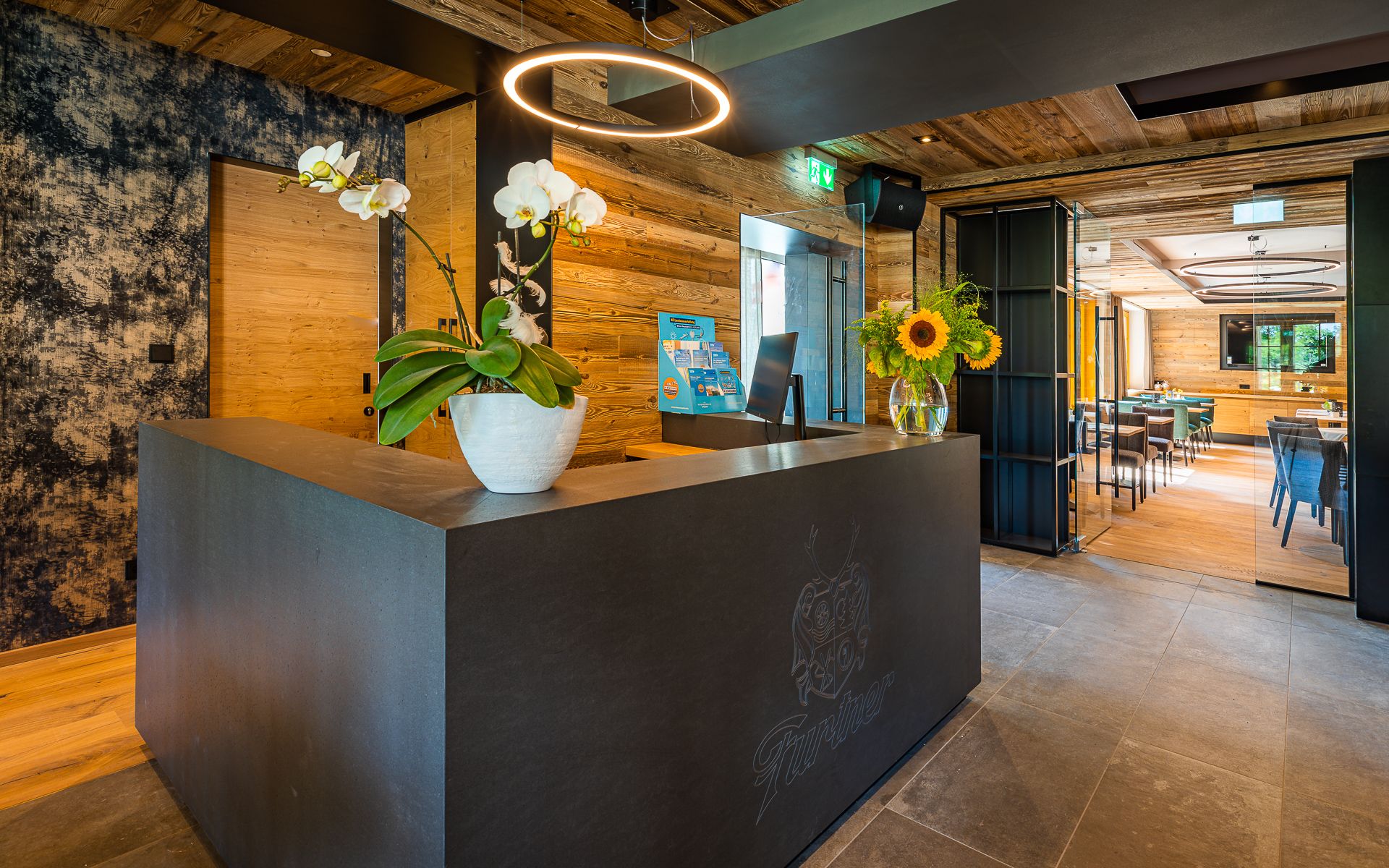 Modern recepció faburkolattal, orchideákkal és napraforgókkal a pulton.