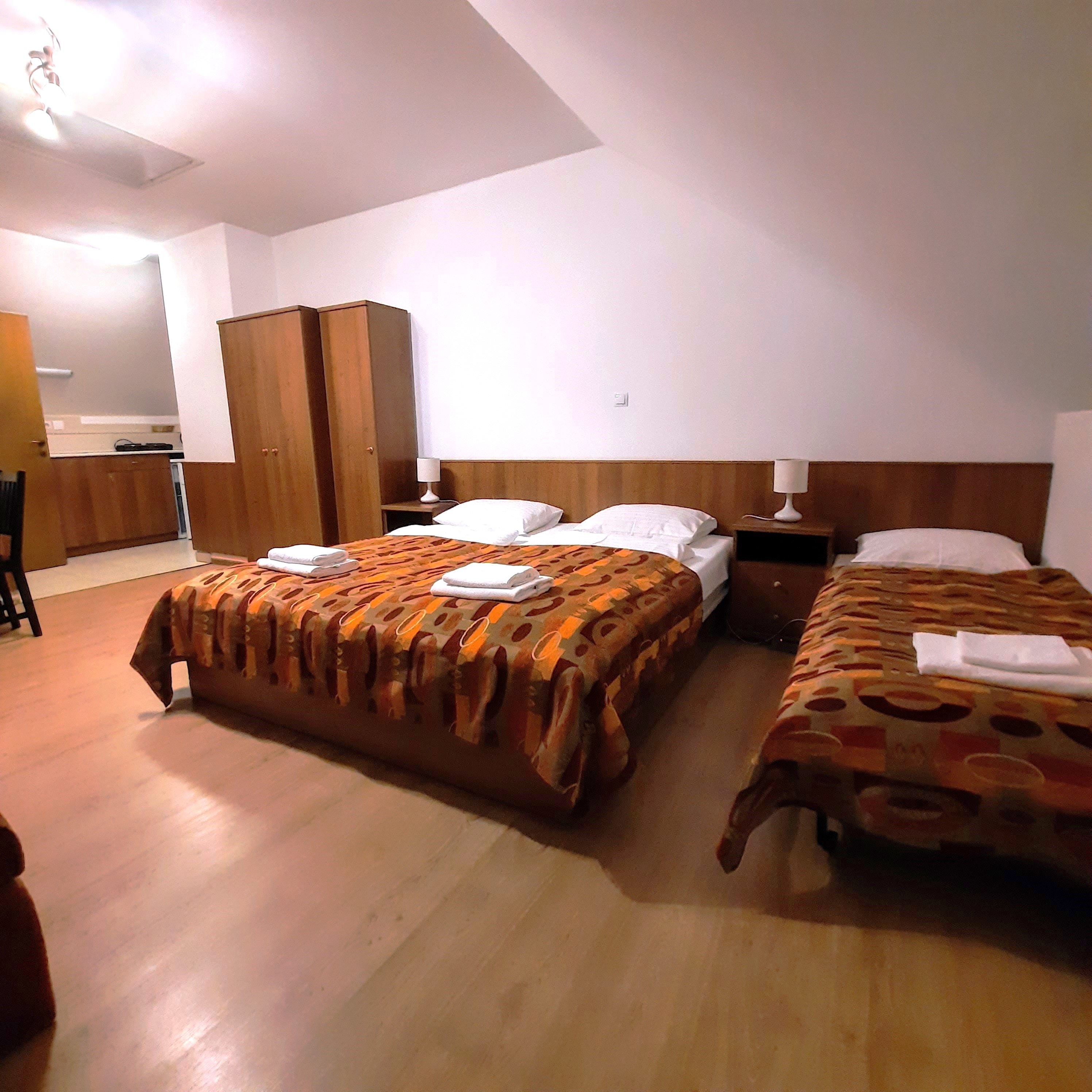 Háromágyas szoba két egyszemélyes ággyal és egy franciaággyal, mindegyik mintás takaróval. Szekrény és éjjeliszekrények is rendelkezésre állnak.