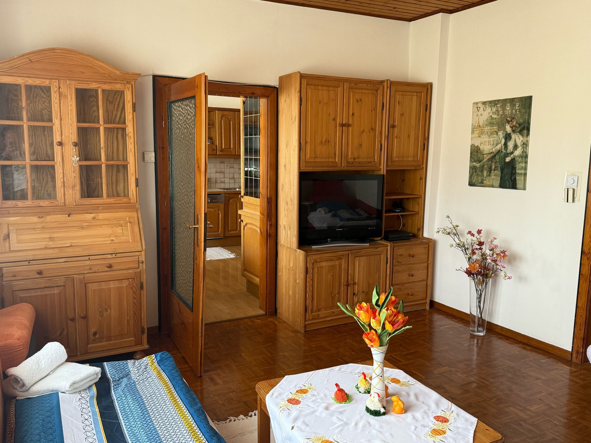 Nappali fából készült bútorokkal, virágokkal díszített asztallal és televízióval.
