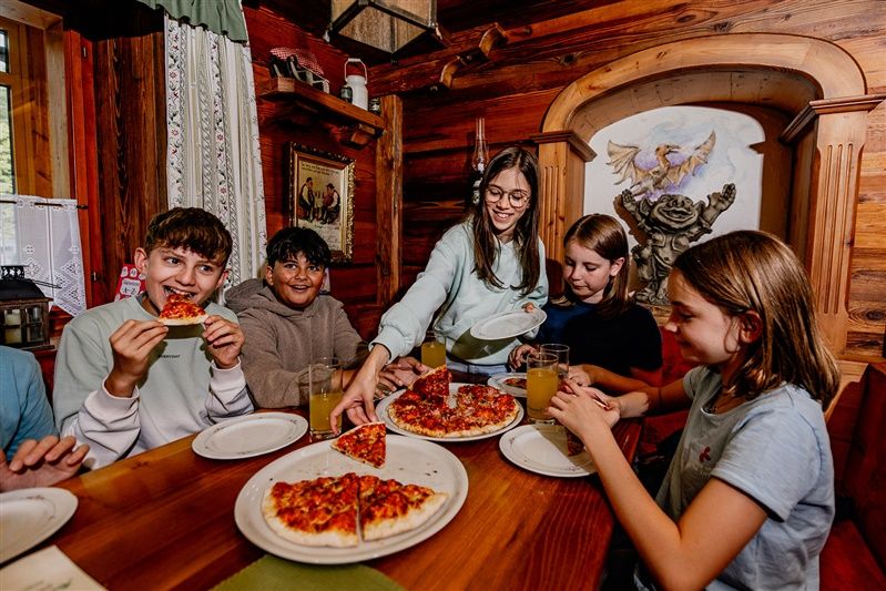 A gyerekek pizzát esznek egy rusztikus, fából készült falú szobában.