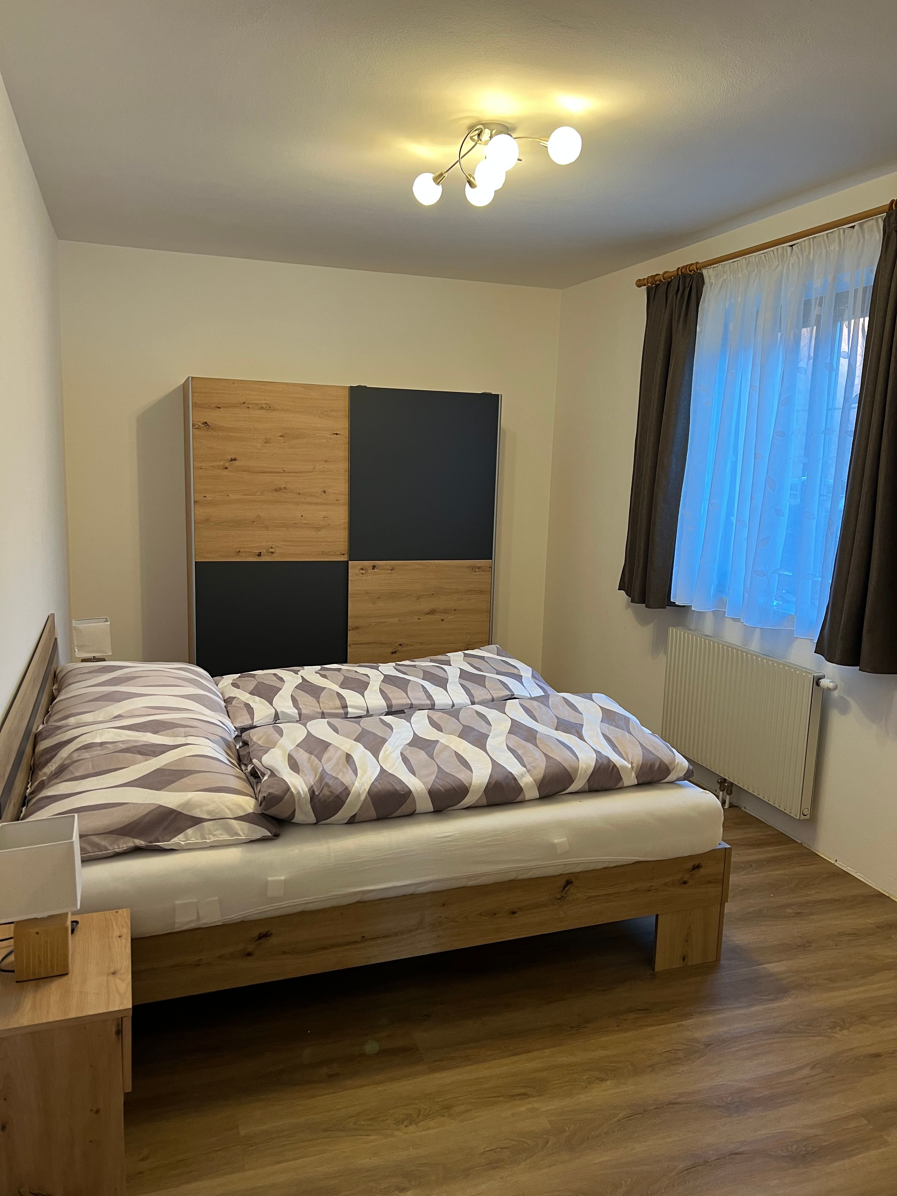 Hangulatos kétágyas szoba faággyal, szekrénnyel és függönyös ablakkal.