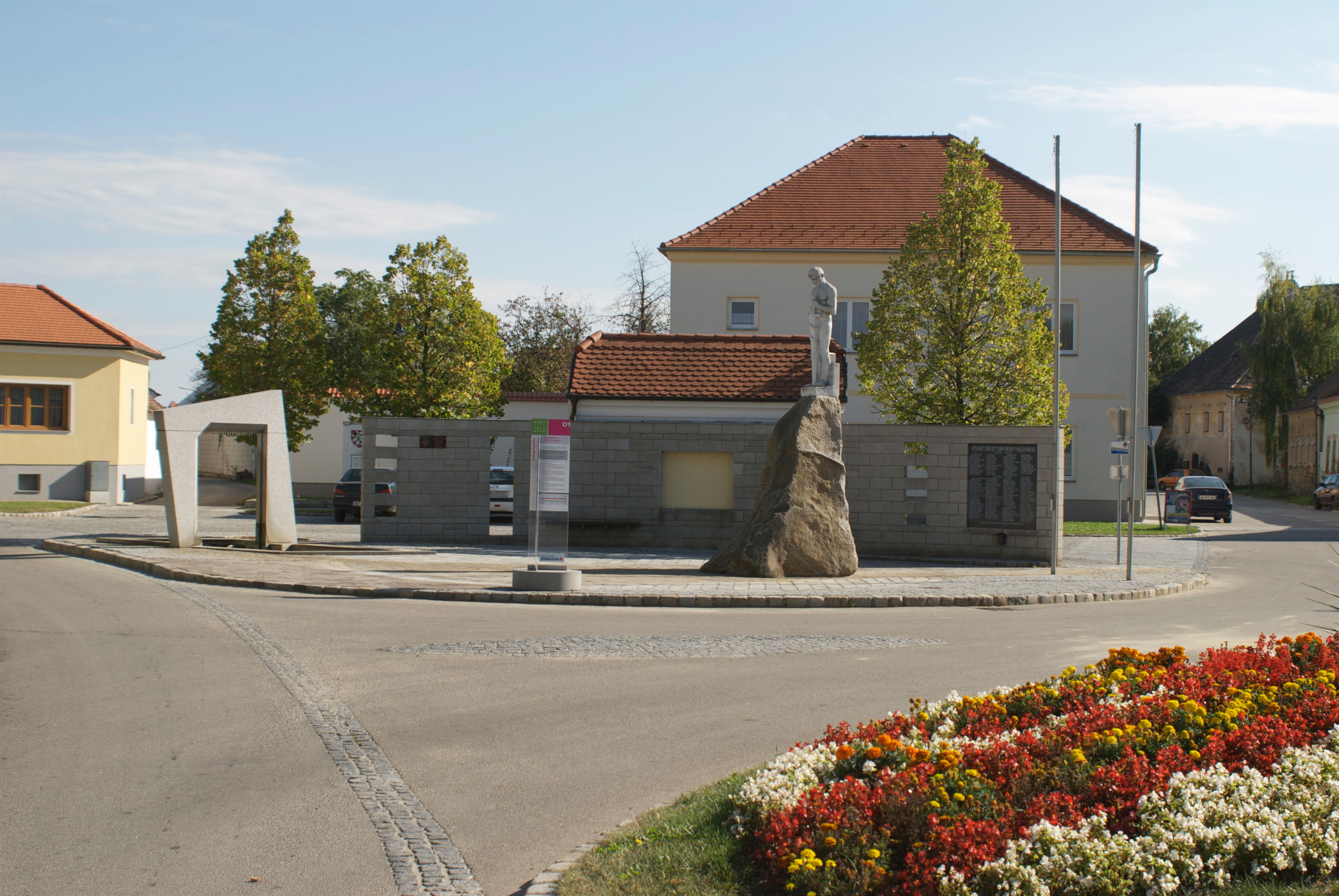 Emlékmű Mailbergben egy sziklán álló szoborral, épületekkel és virágágyásokkal körülvéve.
