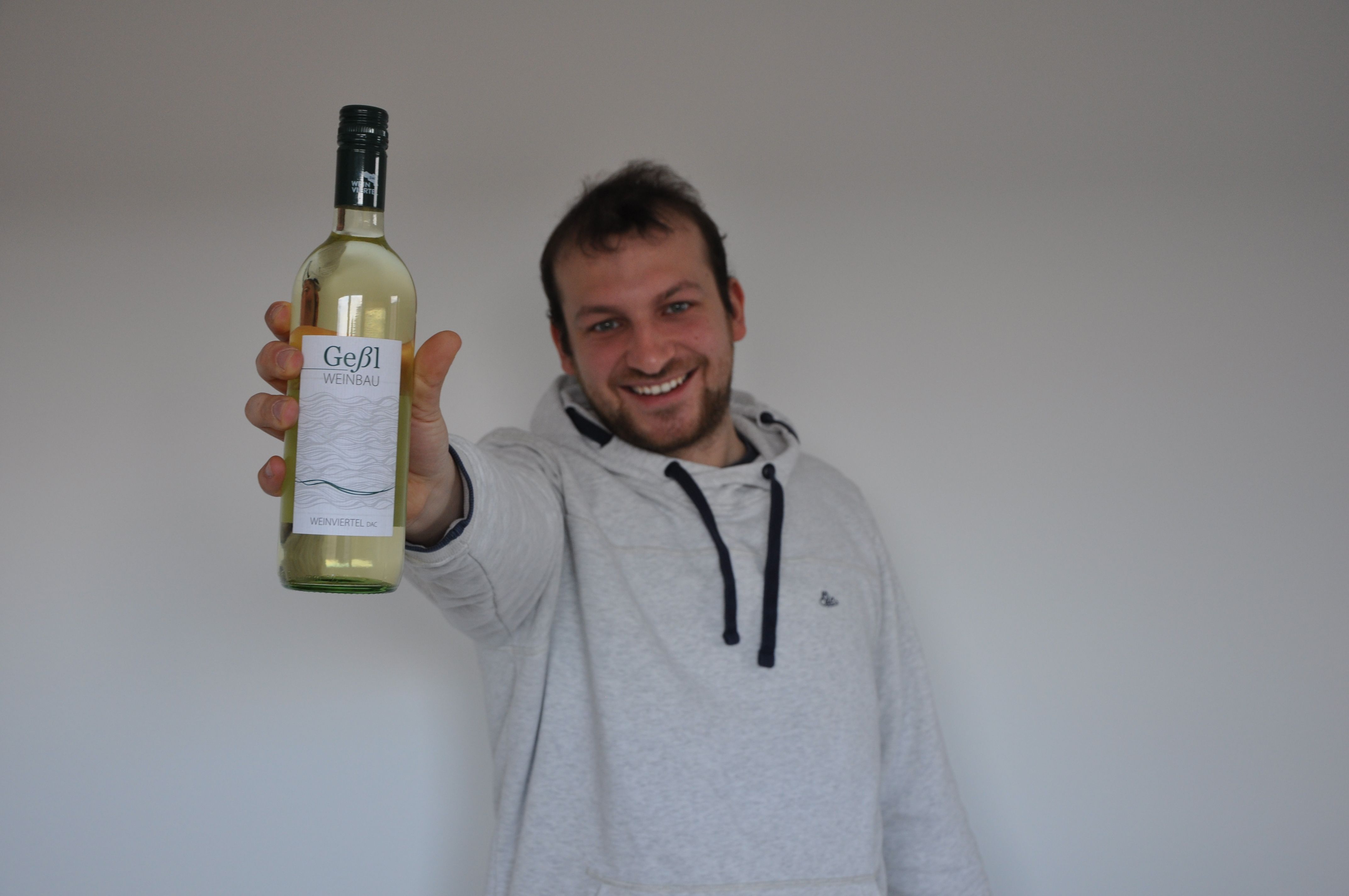 Egy férfi egy üveg Geßl Weinbau fehérbort tart a kamera elé.