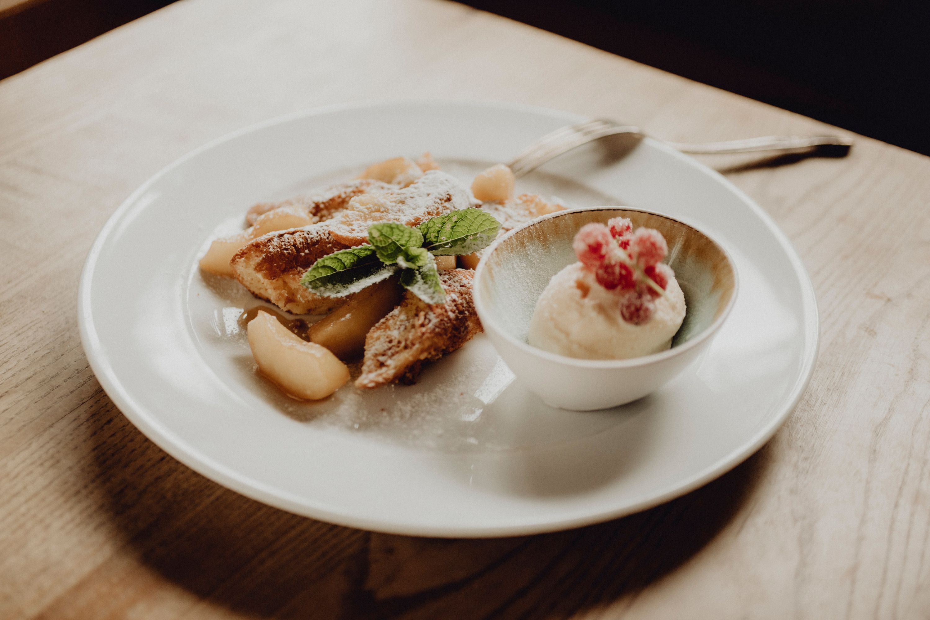 Egy tányér almás palacsinta és egy tál túró rumos fagylalt, mentalevelekkel és piros bogyós gyümölcsökkel díszítve.