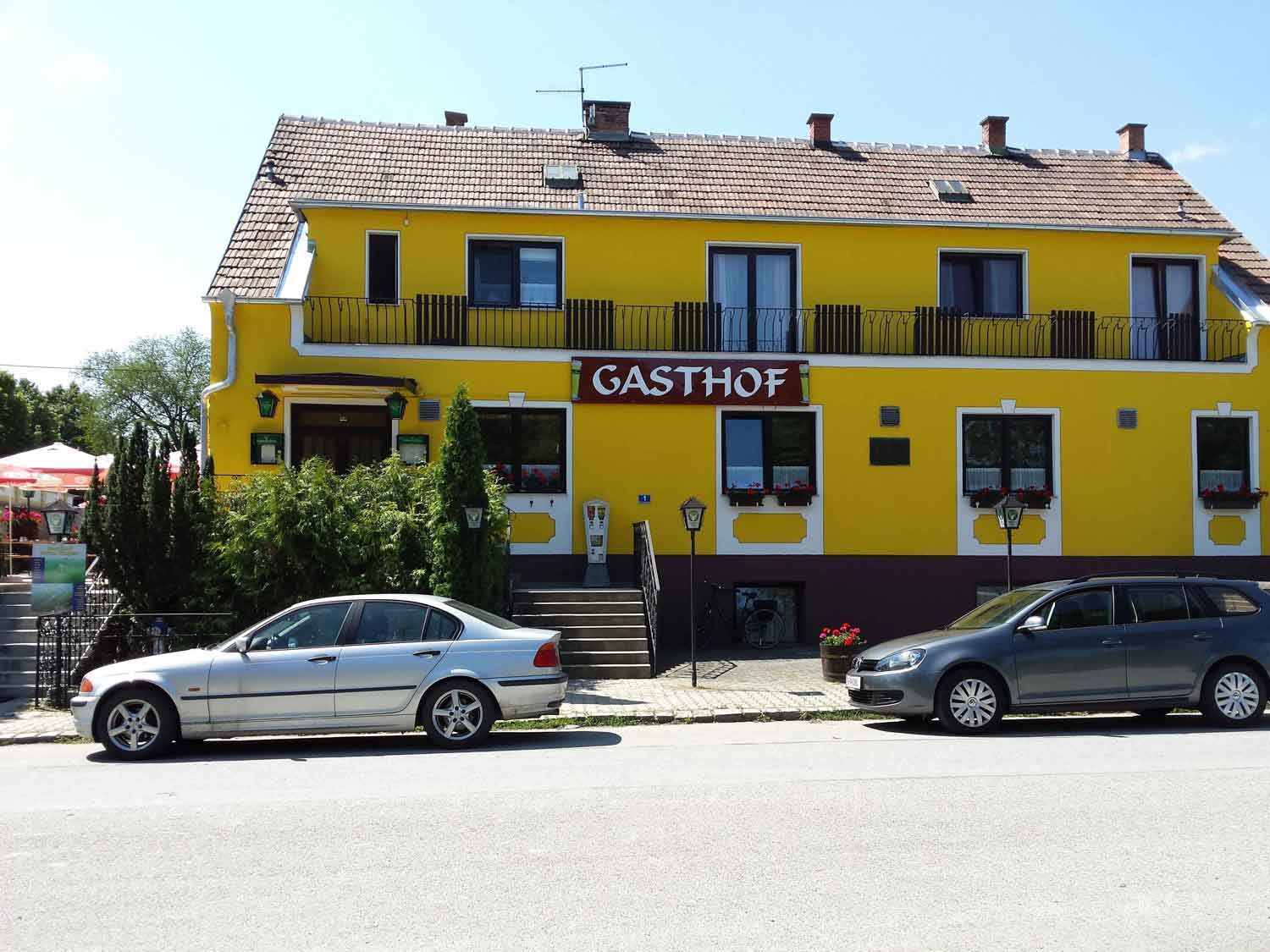 Sárga színű, "Gasthof" feliratú épület, előtte parkoló autók.