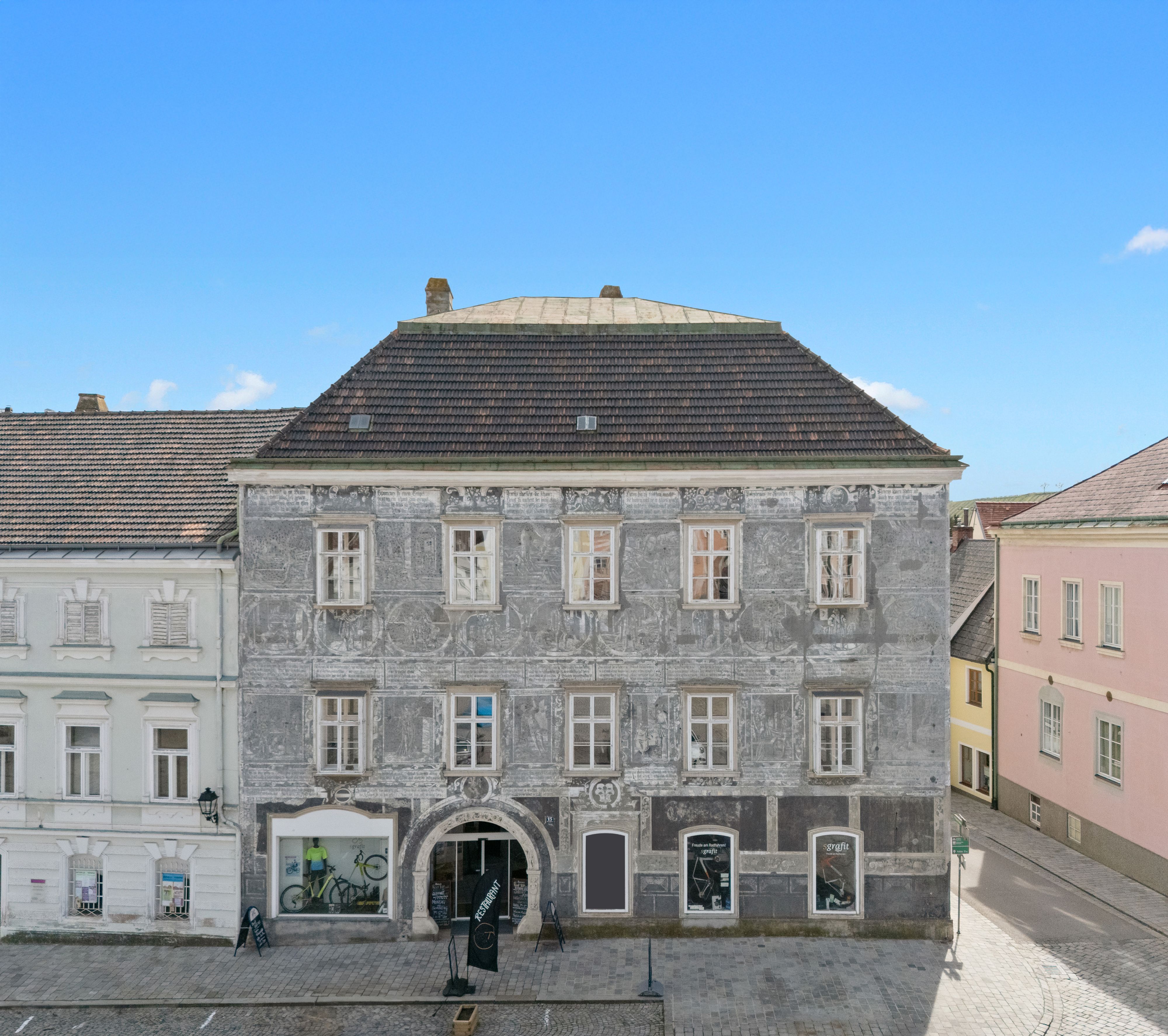 Történelmi épület szürke homlokzattal és díszítő festményekkel egy városban.