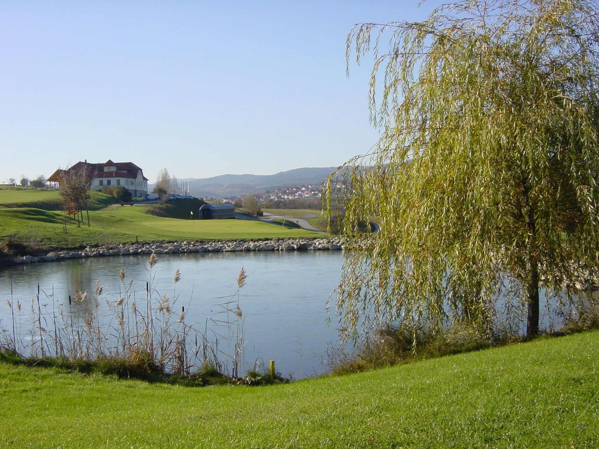 Golfpálya tóval, fákkal és egy épülettel a háttérben.