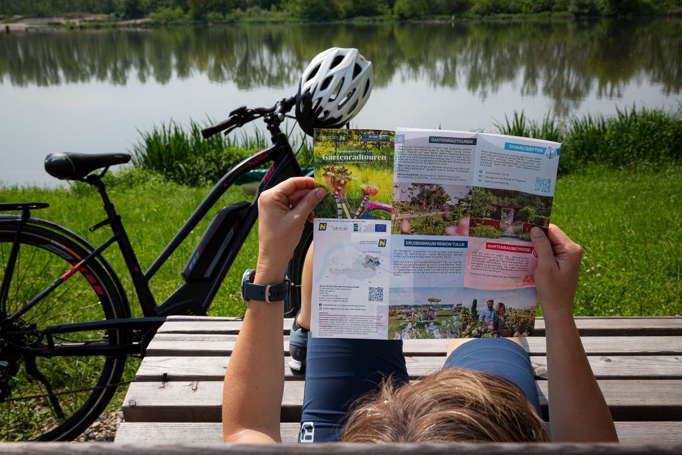 Egy személy egy kerti kerékpártúrákról szóló kihajtható térképet olvas a tó melletti kerékpár mellett.