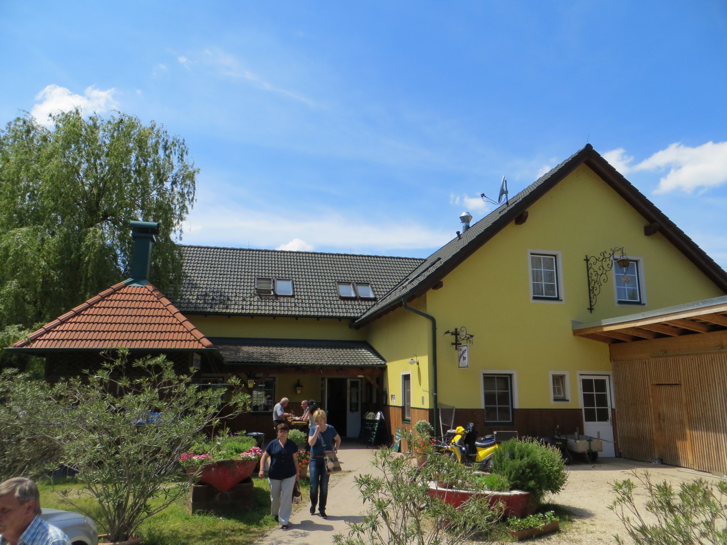Sárga vendéglő szürke tetővel és kerttel az előtérben.