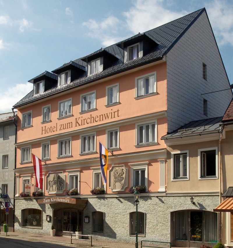 A Hotel zum Kirchenwirt homlokzata zászlókkal és kék éggel.