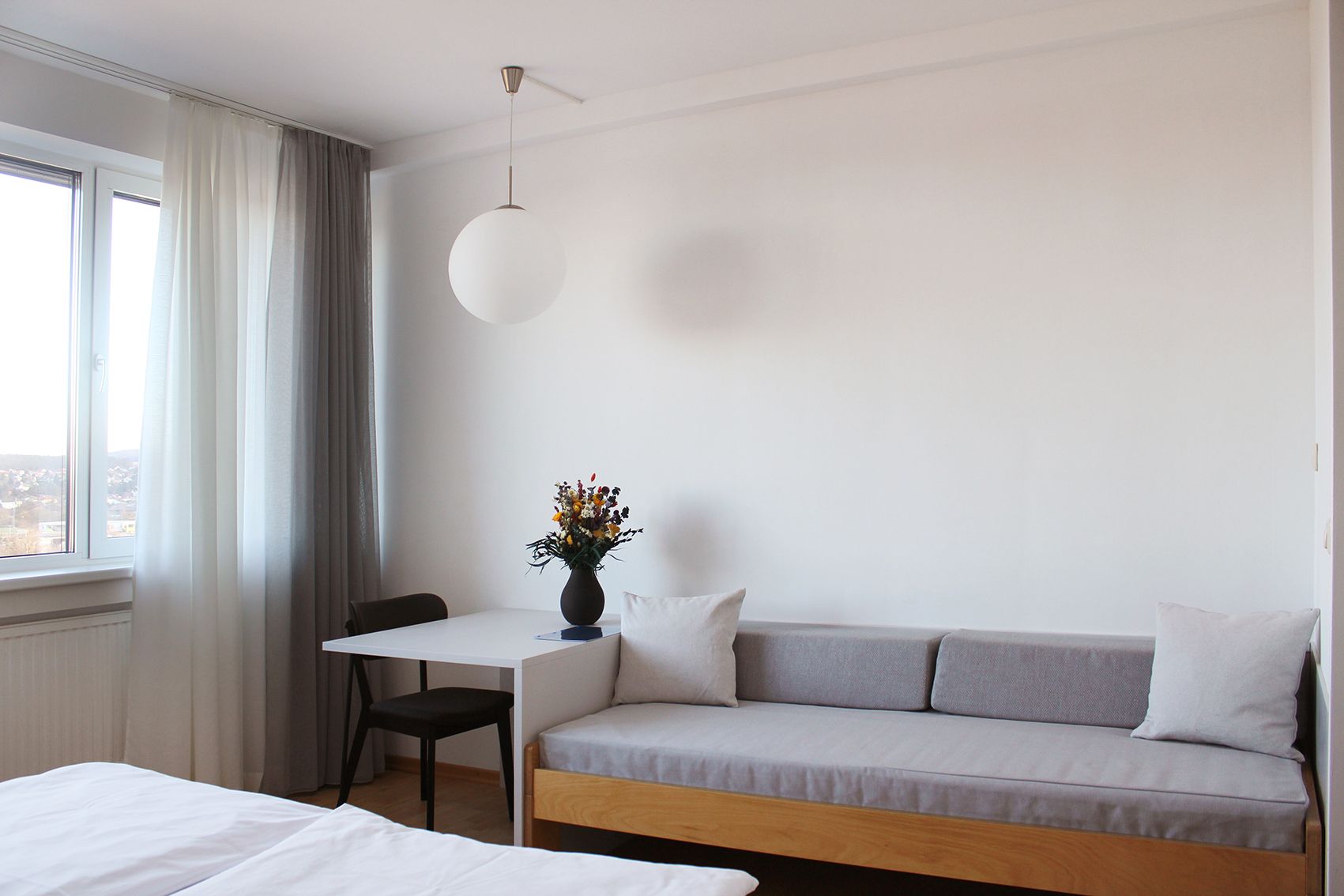 Modern vendégszoba kanapéval, asztallal, székkel és függönyös ablakkal.