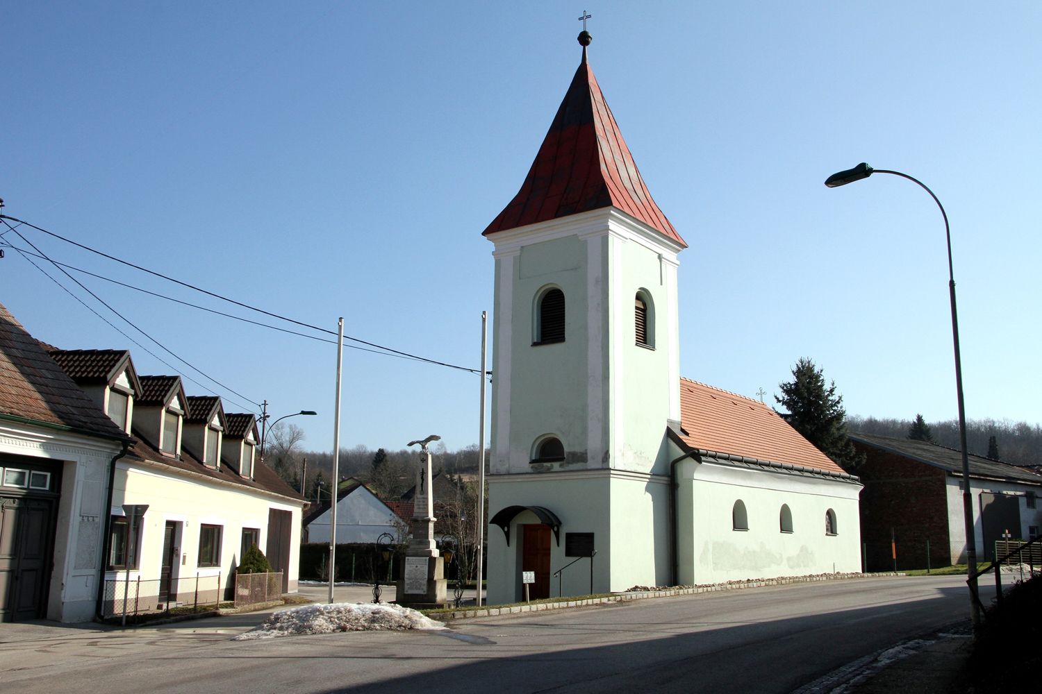 Piros tetős templom és torony egy faluban, tiszta ég alatt.