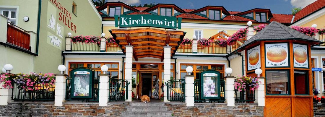 A Kirchenwirt étterem bejárata virágokkal és táblákkal.