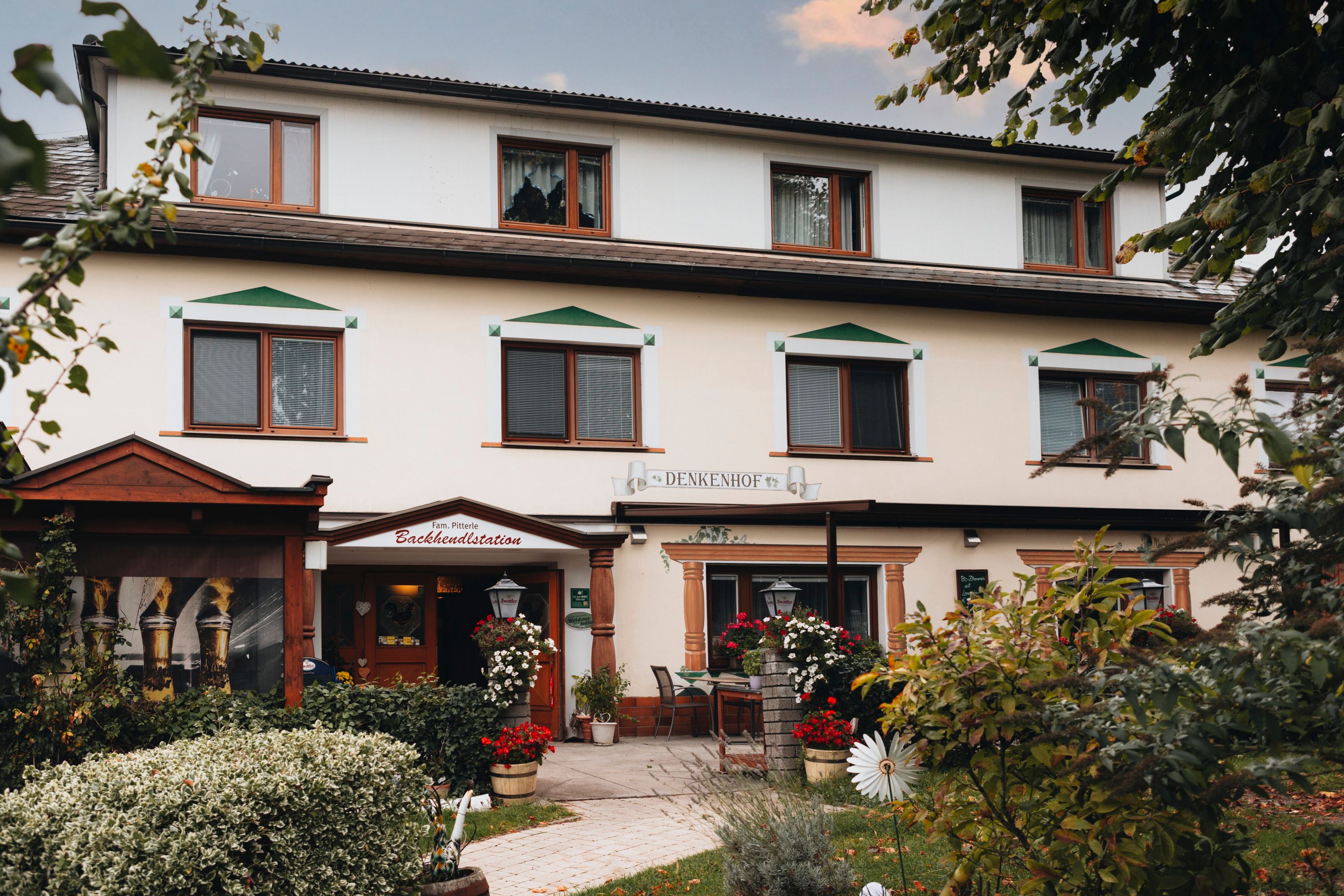 Egy hagyományos fogadó, virágokkal és fákkal az előtérben.