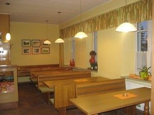 Egy hangulatos kávézó belső nézete, fa asztalokkal és padokkal, képekkel és növényekkel díszítve.