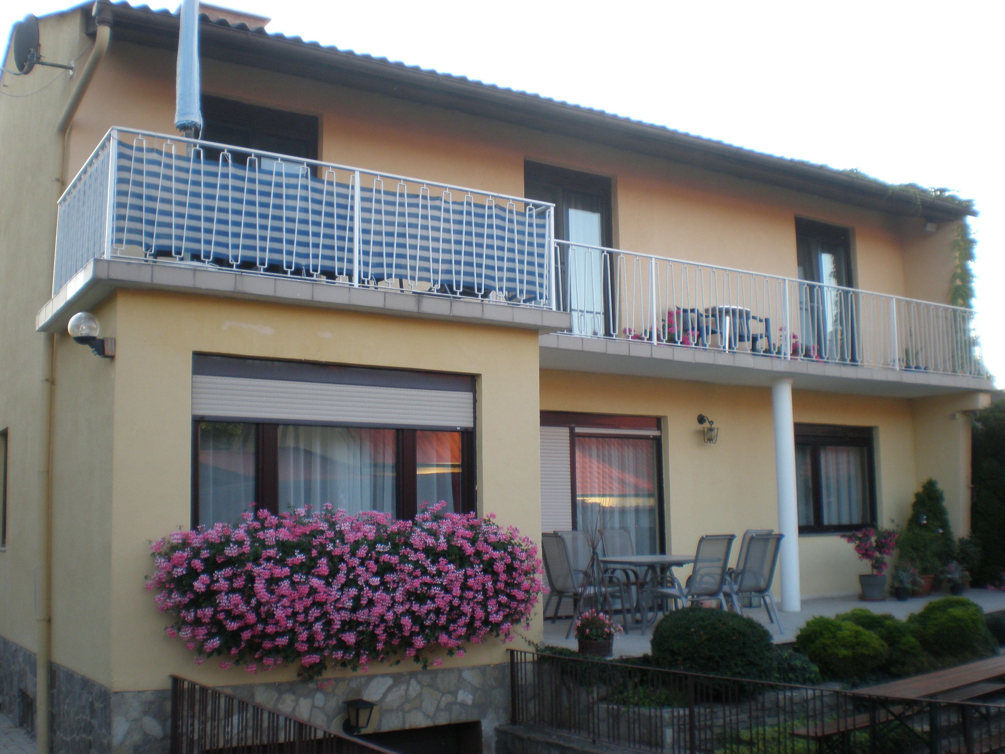 Kétszintes ház erkéllyel, virágokkal és kerti bútorokkal.