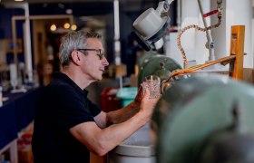 Egy f&eacute;rfi egy műhelyben egy csiszol&oacute;g&eacute;pen dolgozik egy &uuml;vegen.