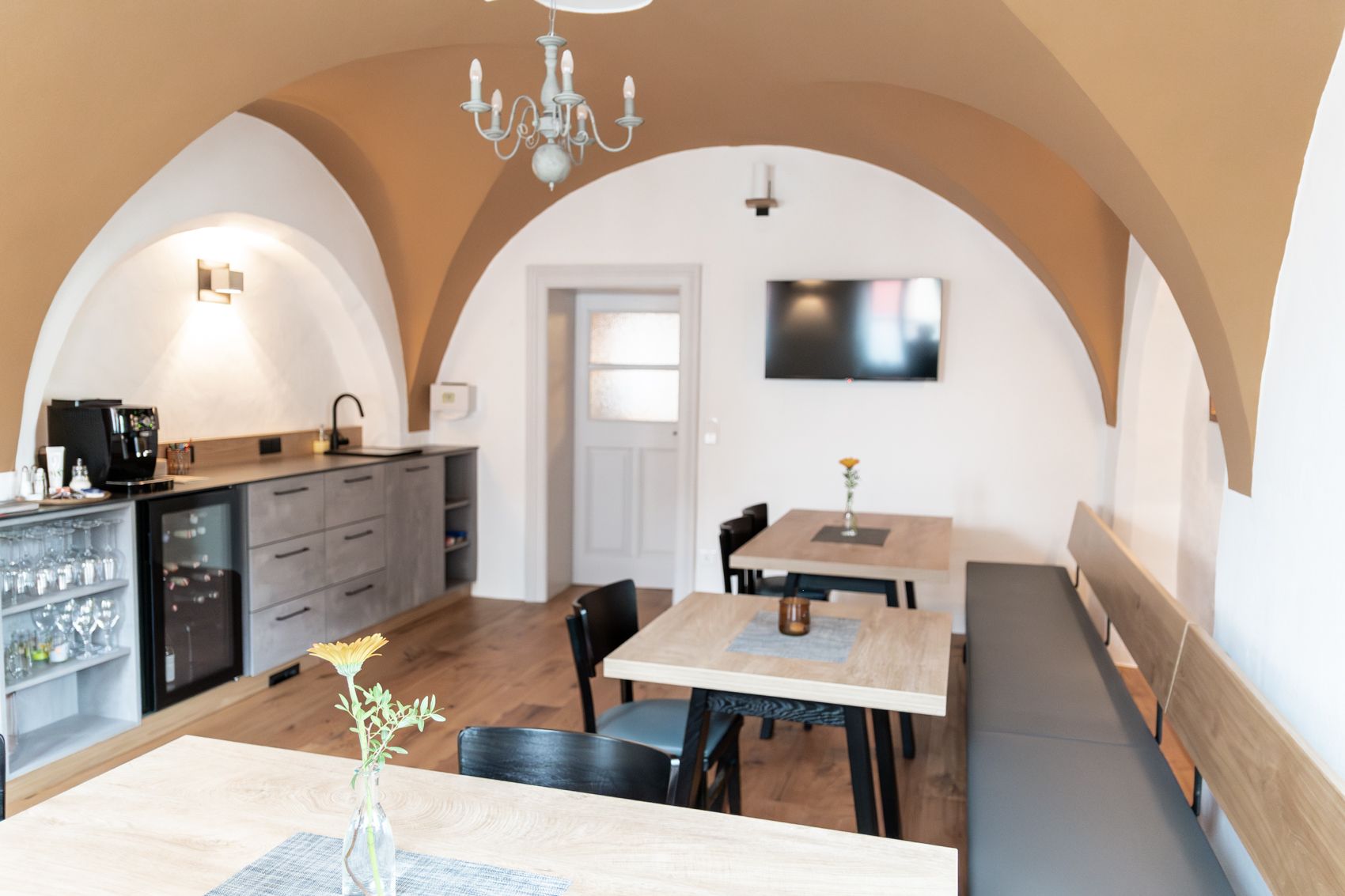 Hangulatos reggelizőterem fa asztalokkal, székekkel és paddal. A falon egy TV függ, és van egy konyhasarok kávéfőzővel.