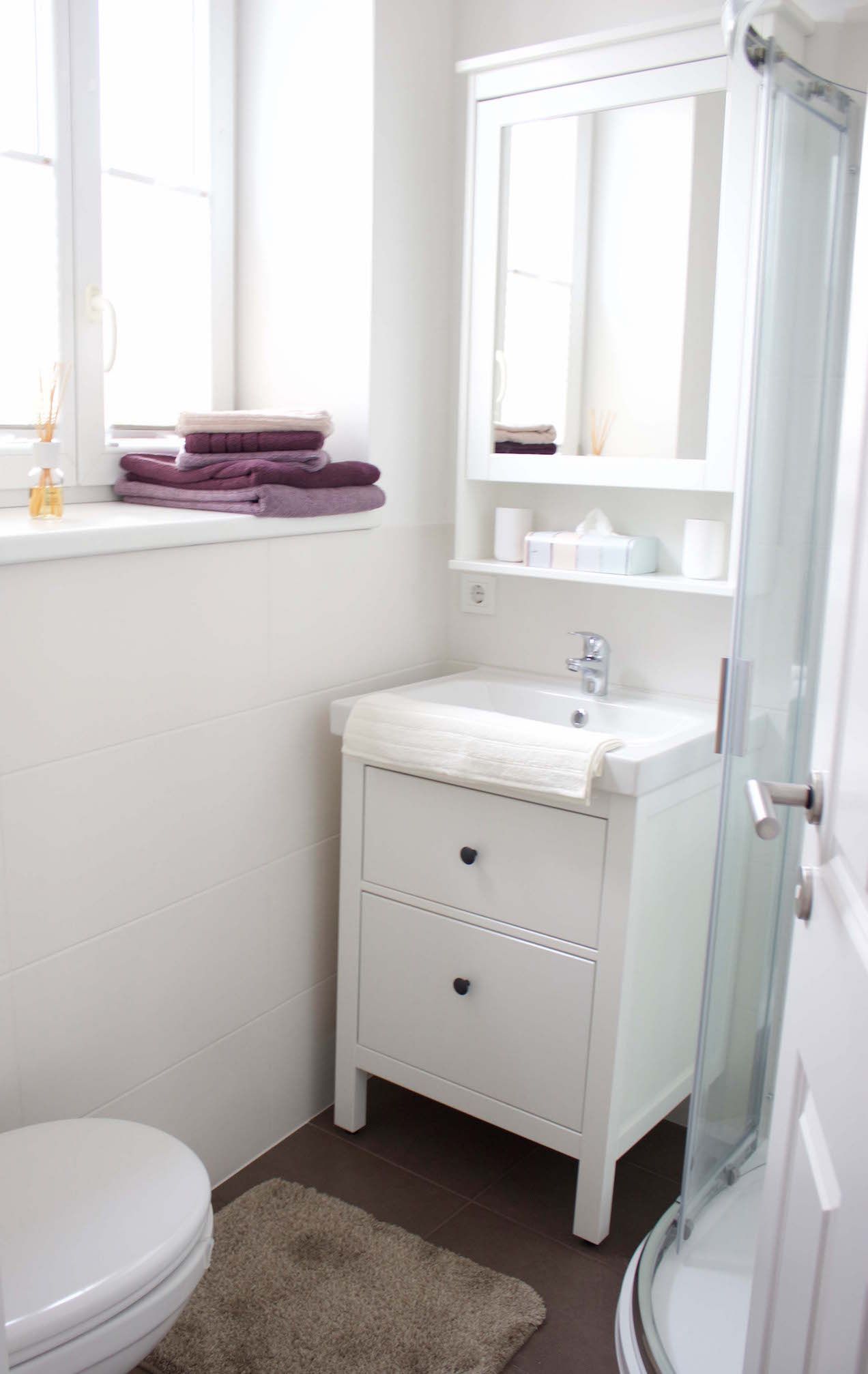 Modern fürdőszoba fehér mosdóval, tükörrel, törölközőkkel és zuhanyzóval.