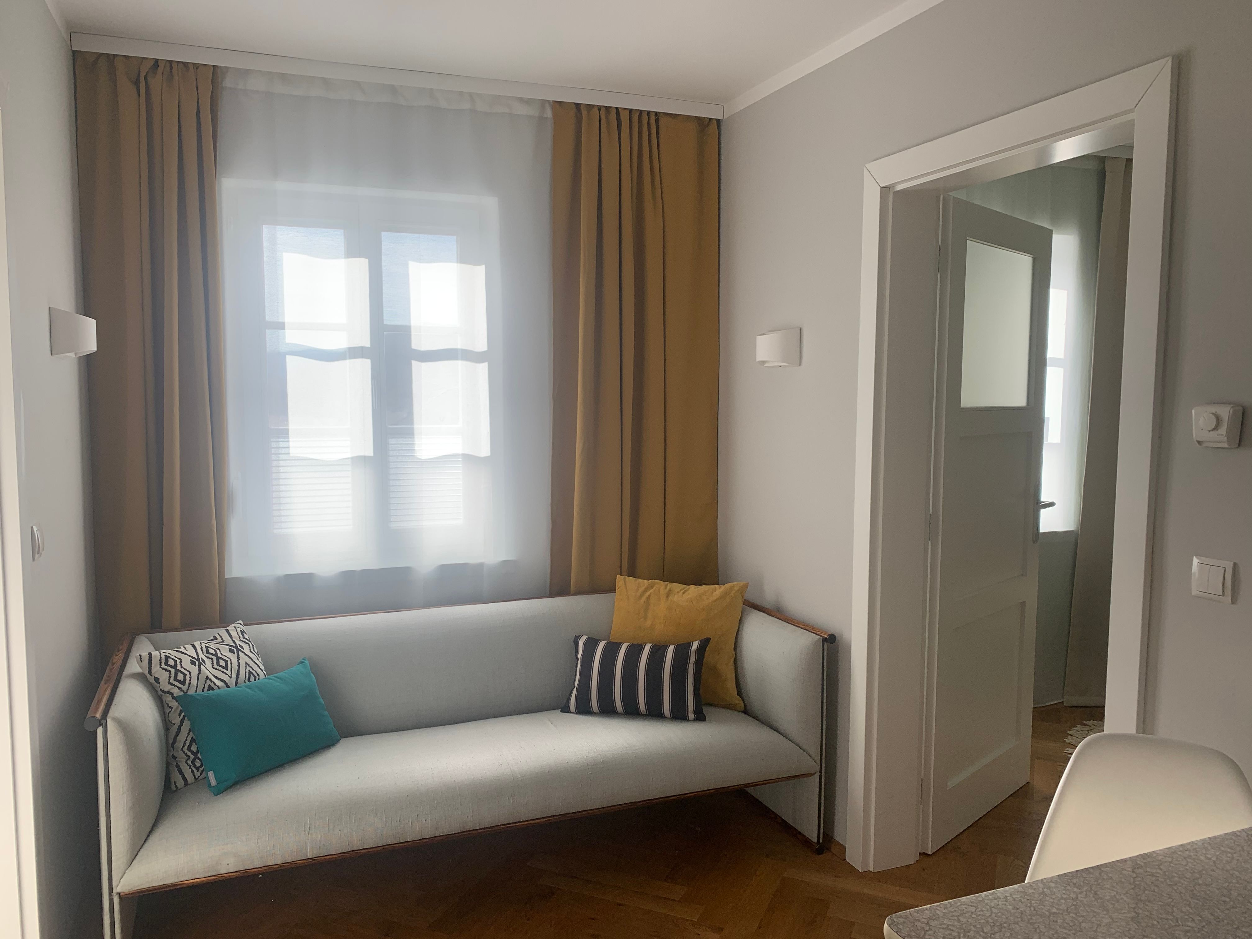 Hangulatos nappali kanapéval és párnákkal, sárga függönyökkel és nyitott ajtókerettel.