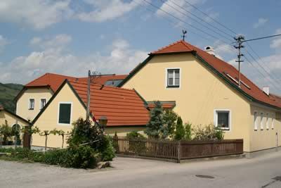 Sárga ház piros tetővel vidéki környezetben.