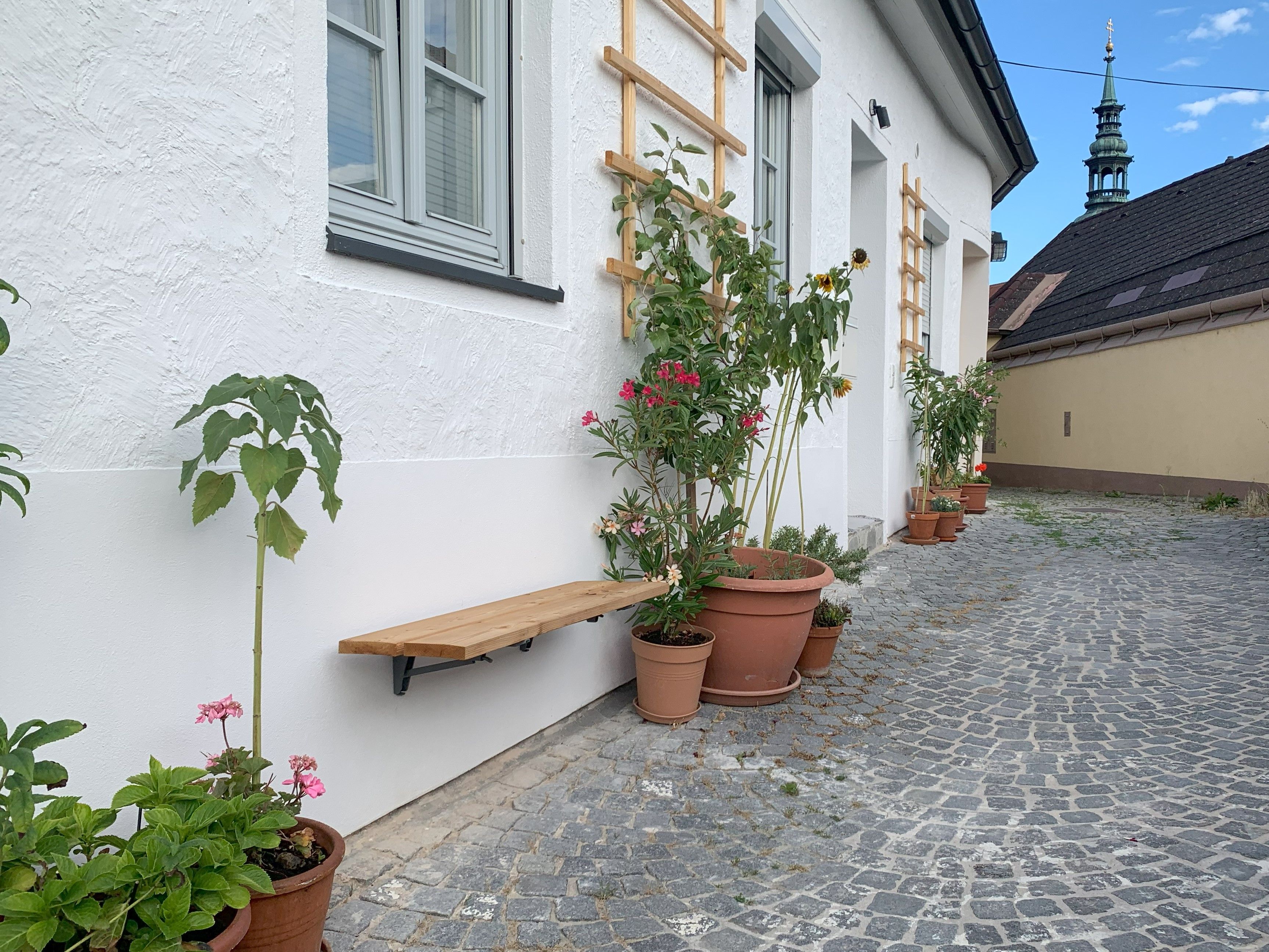 Kövezett út cserepes növényekkel egy fehér épület előtt.