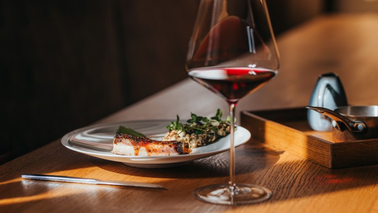 Egy tányér bárányhas, saláta és wasabikrém egy pohár vörösbor mellett egy faasztalon.