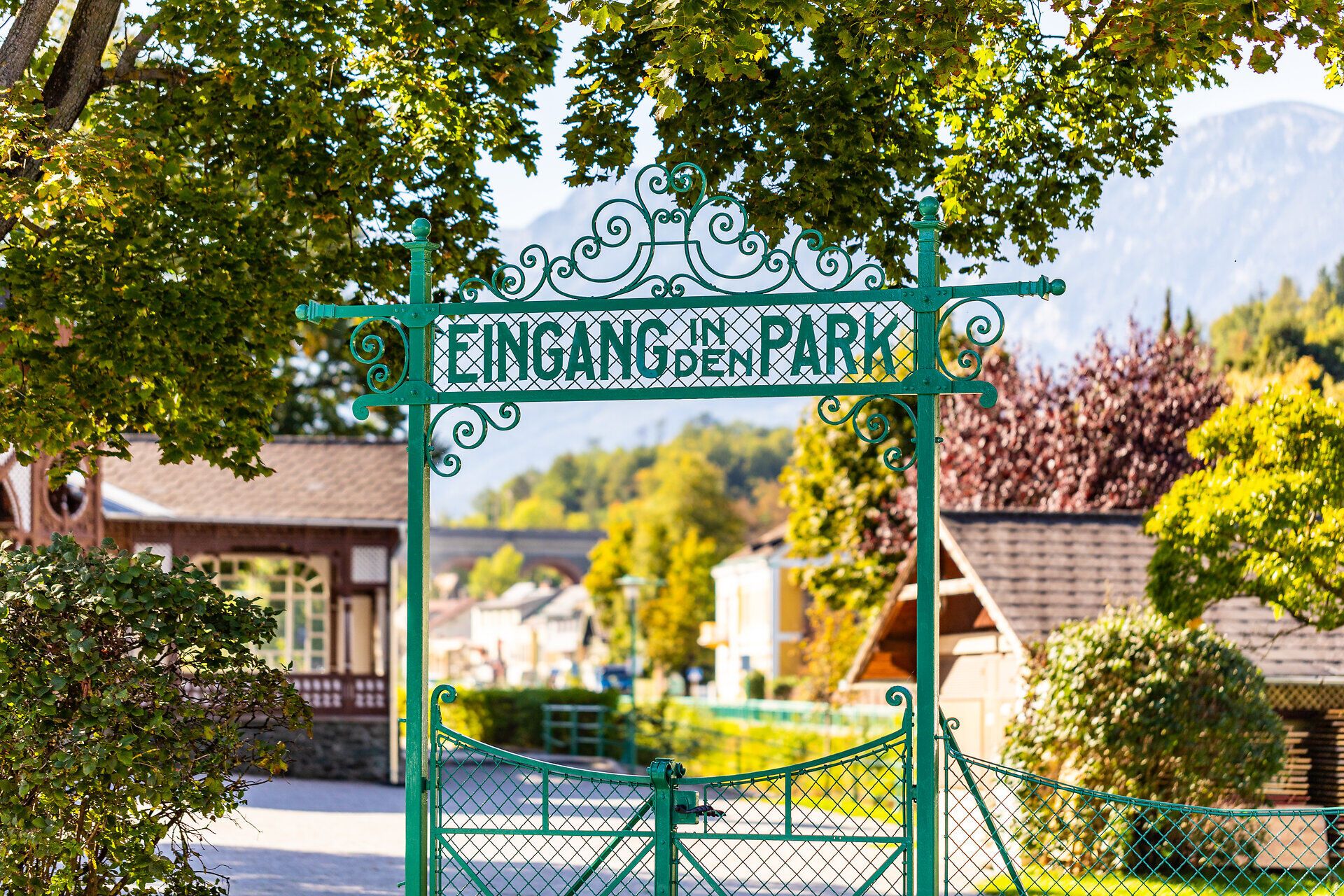 Zöld kapu a "Bejárat a parkba" felirattal, a háttérben a pavilon és a Rax látható.