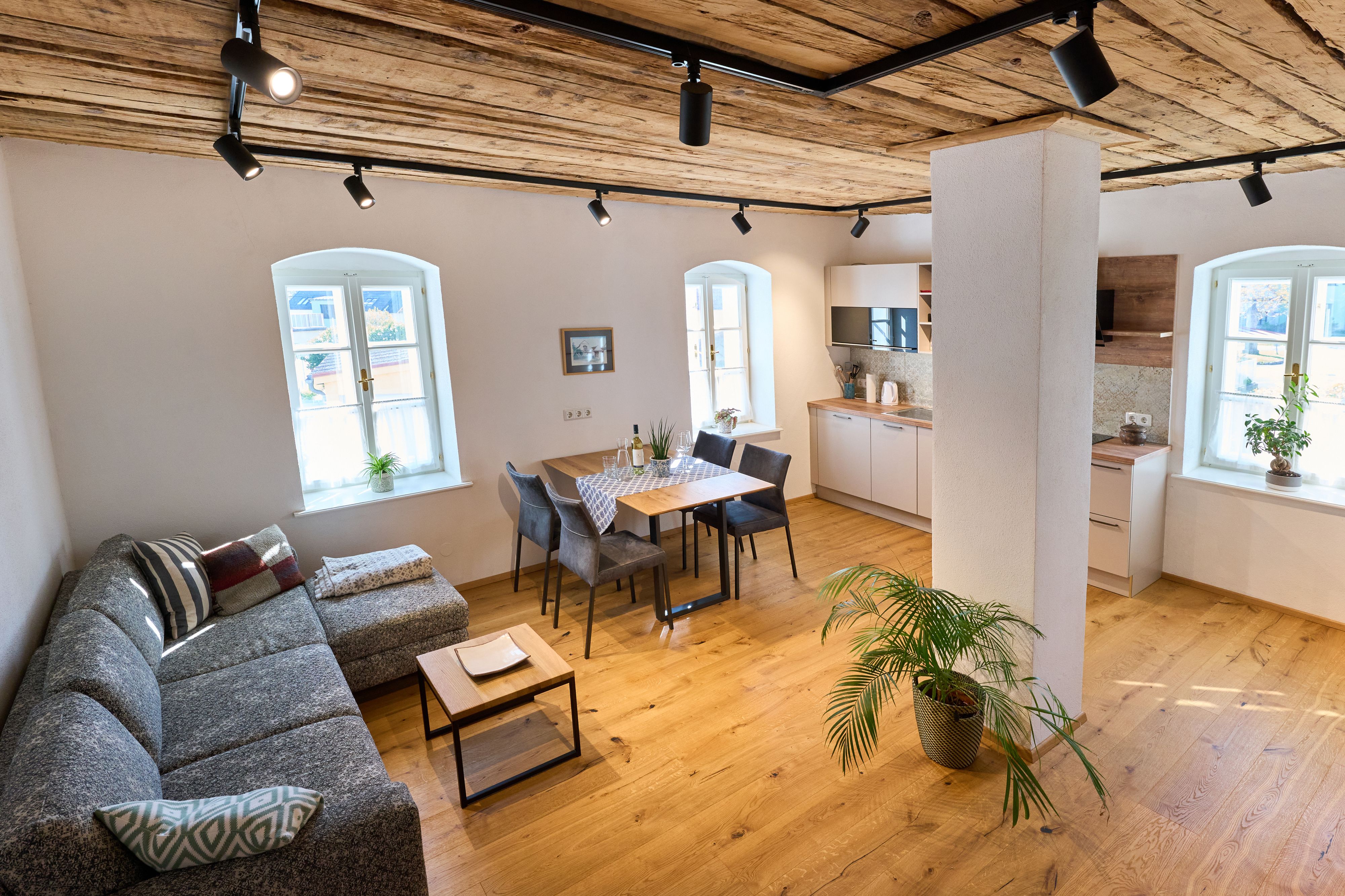 Modern nappali fapadlóval, szürke kanapéval, étkezőasztallal és konyhával.