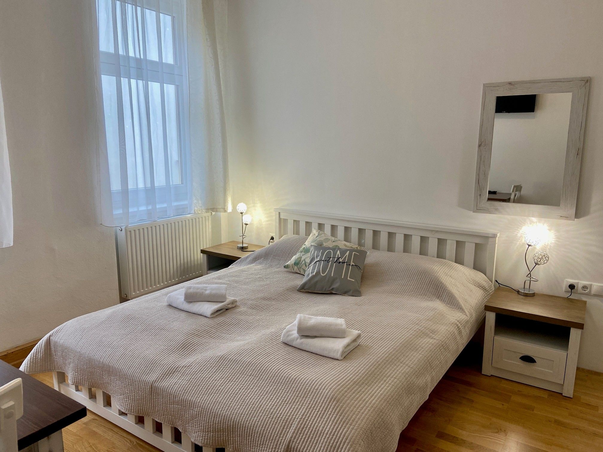 Hangulatos kétágyas szoba nagy ággyal, két éjjeliszekrénnyel és egy tükörrel a falon. A szoba világos és hívogató.