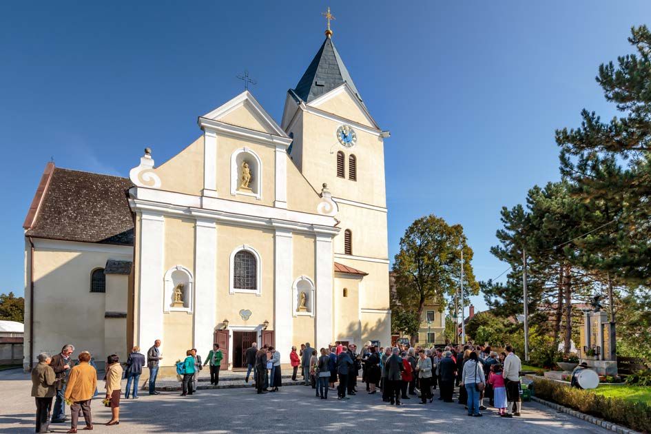 Emberek gyűlnek össze egy tornyos templom és egy óra előtt napsütéses időben.