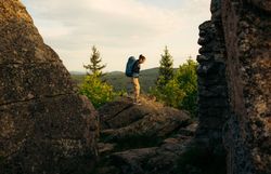 Eine Frau stehen zwischen imposanten Felsformationen und geht gerade weiter, hinter ihr die Weite des Waldviertels mit der Waldlandschaft 