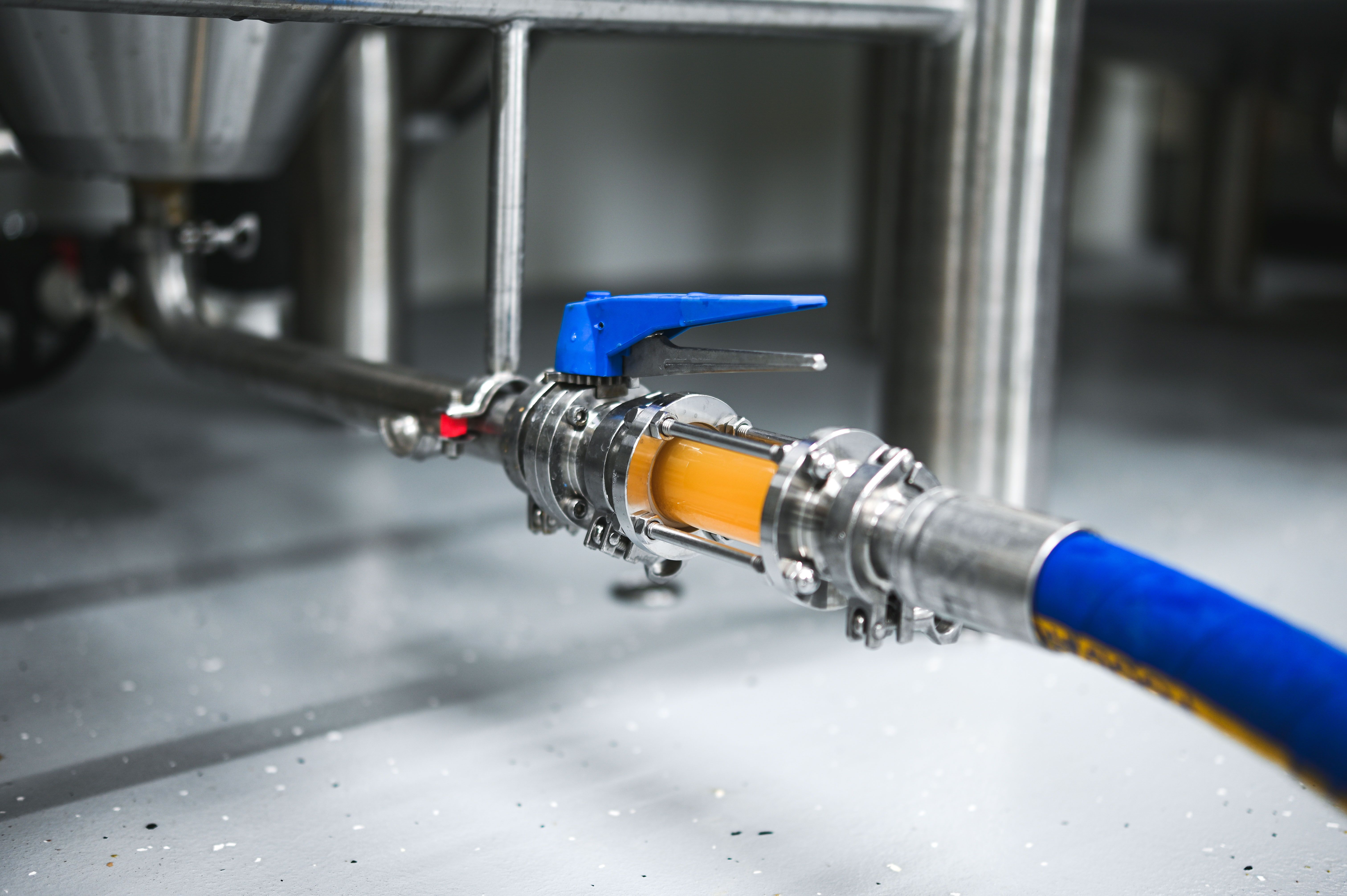 Közelkép egy sörgyári tömlőről szeleppel és a rajta átfolyó folyadékkal.