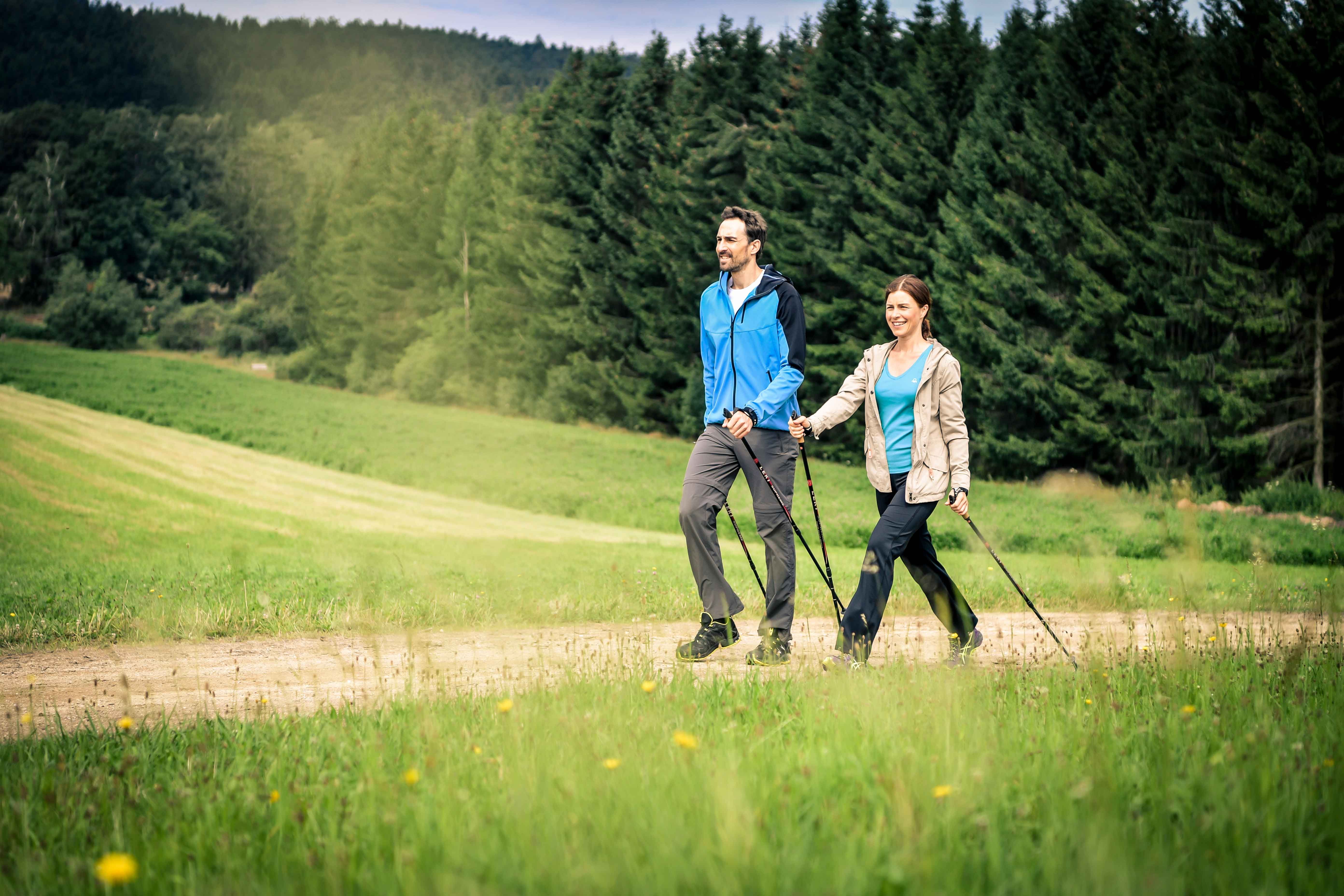 Egy pár nordic walking egy erdő előtti országúton.