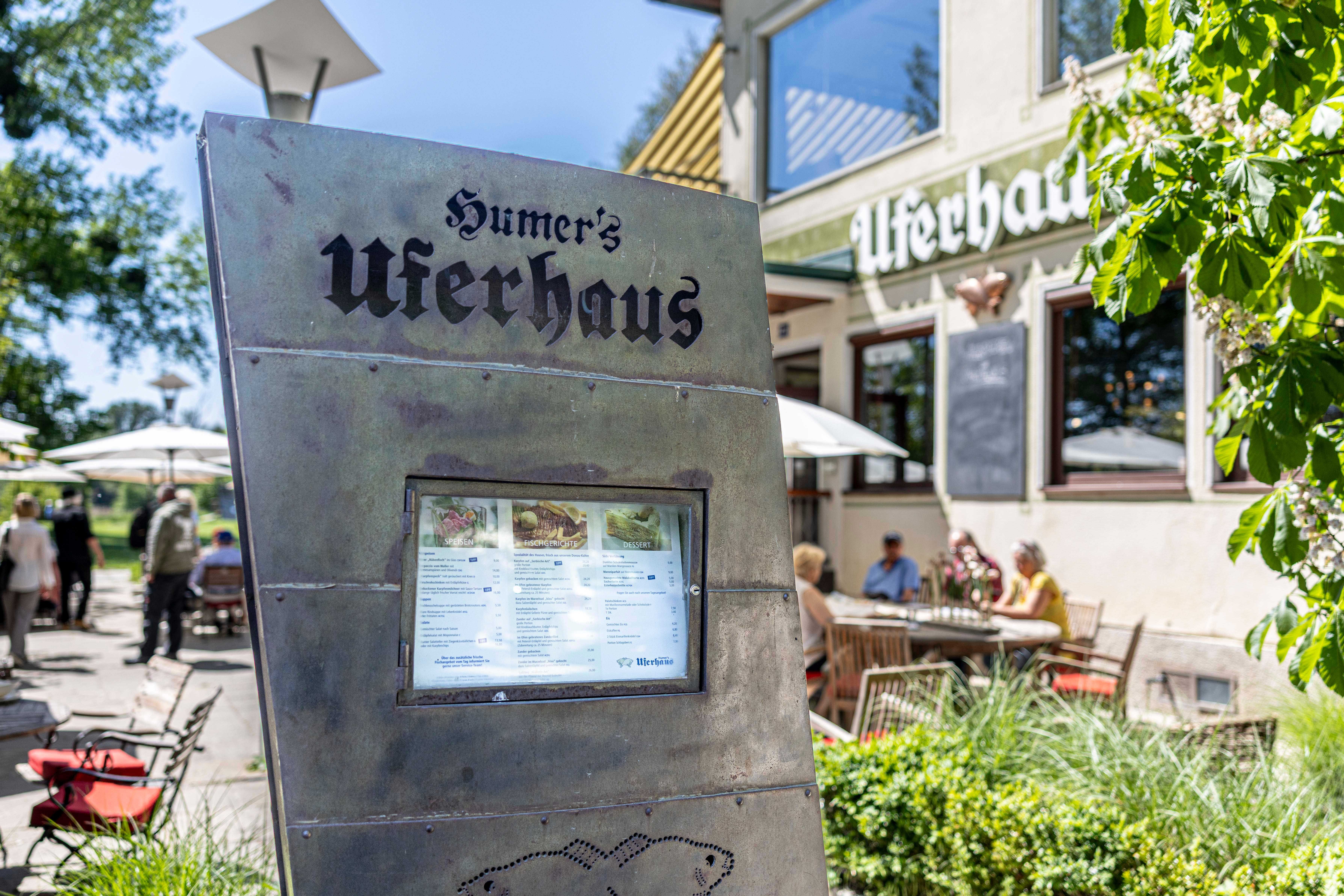 A Humer's Uferhaus külső nézete, előtérben az étlap, háttérben a vendégek.