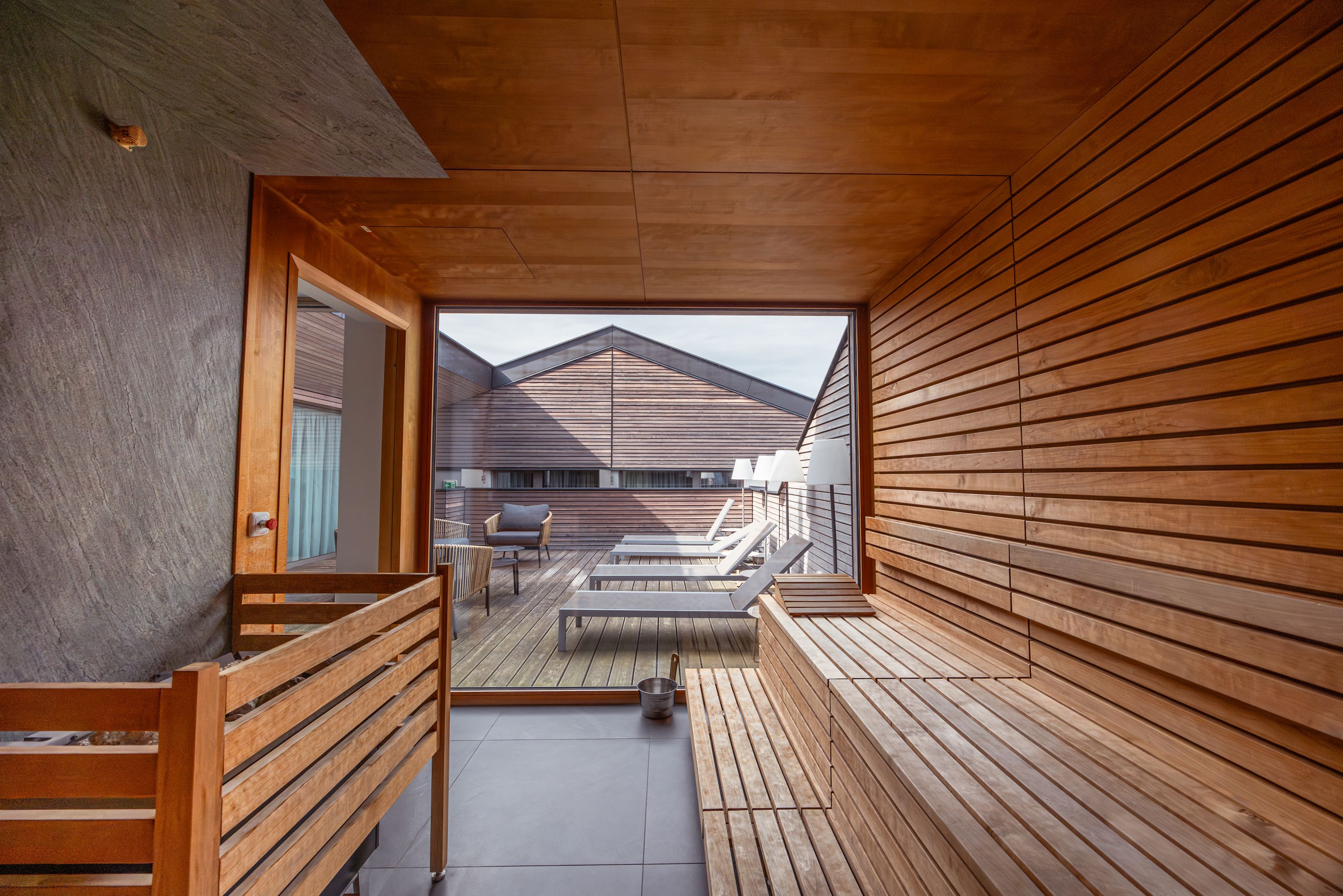 Egy szauna belső nézete, amely egy nyugágyakkal és fából készült falakkal ellátott teraszra néz.