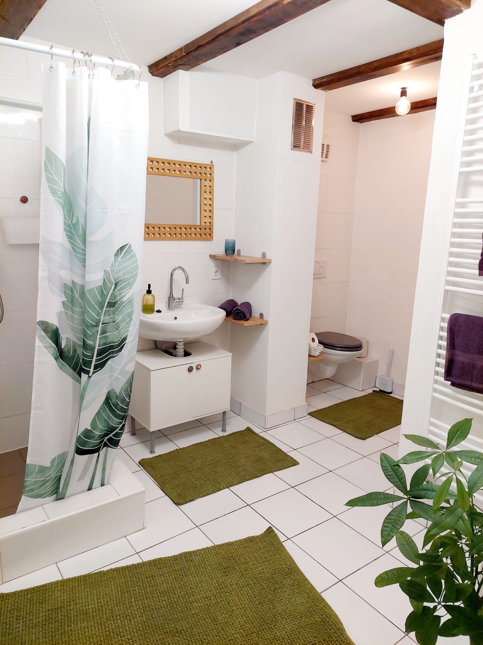 Modern fürdőszoba fehér csempével, zöld szőnyeggel és növényi motívumos zuhanyfüggönnyel.