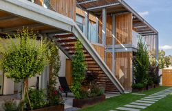 Modern épület fehér homlokzattal és fa elemekkel, fakerítéssel körülvett fal, fa kapuval.