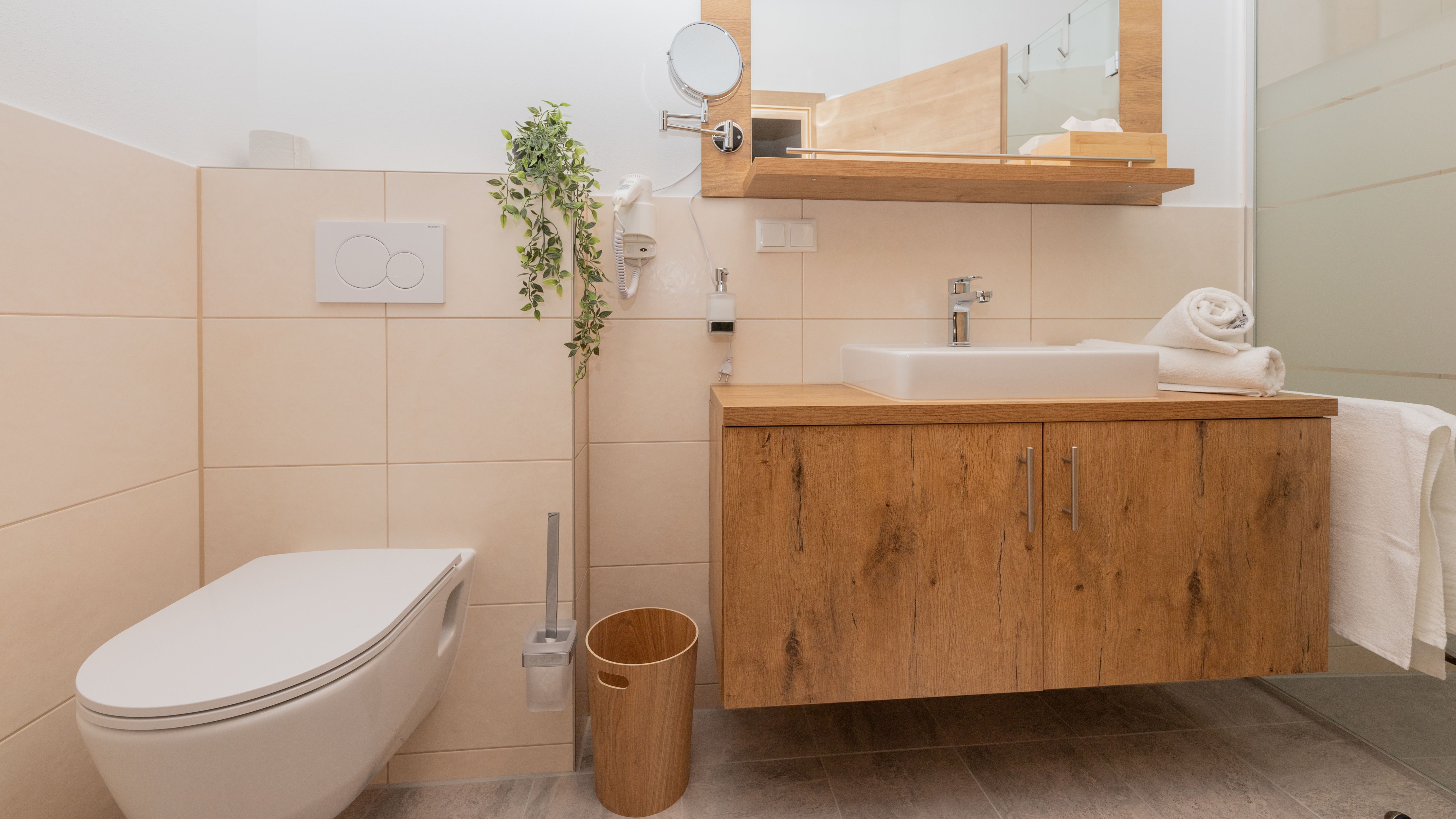 Modern fürdőszoba fából készült mosdóval, mosdókagylóval, WC-vel és törölközőkkel.