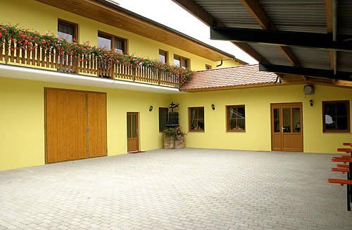 Egy sárga épület belső udvara, faajtókkal és virágokkal díszített erkéllyel.