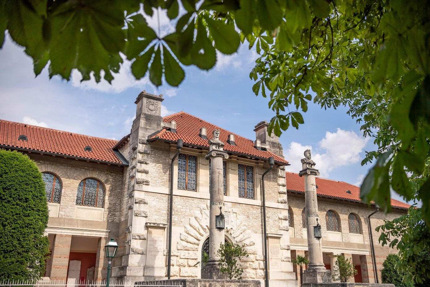 A Bad Deutsch-Altenburg-i Carnuntinum Múzeum külső nézete oszlopokkal és vörös cseréptetővel, zöld fákkal körülvéve.