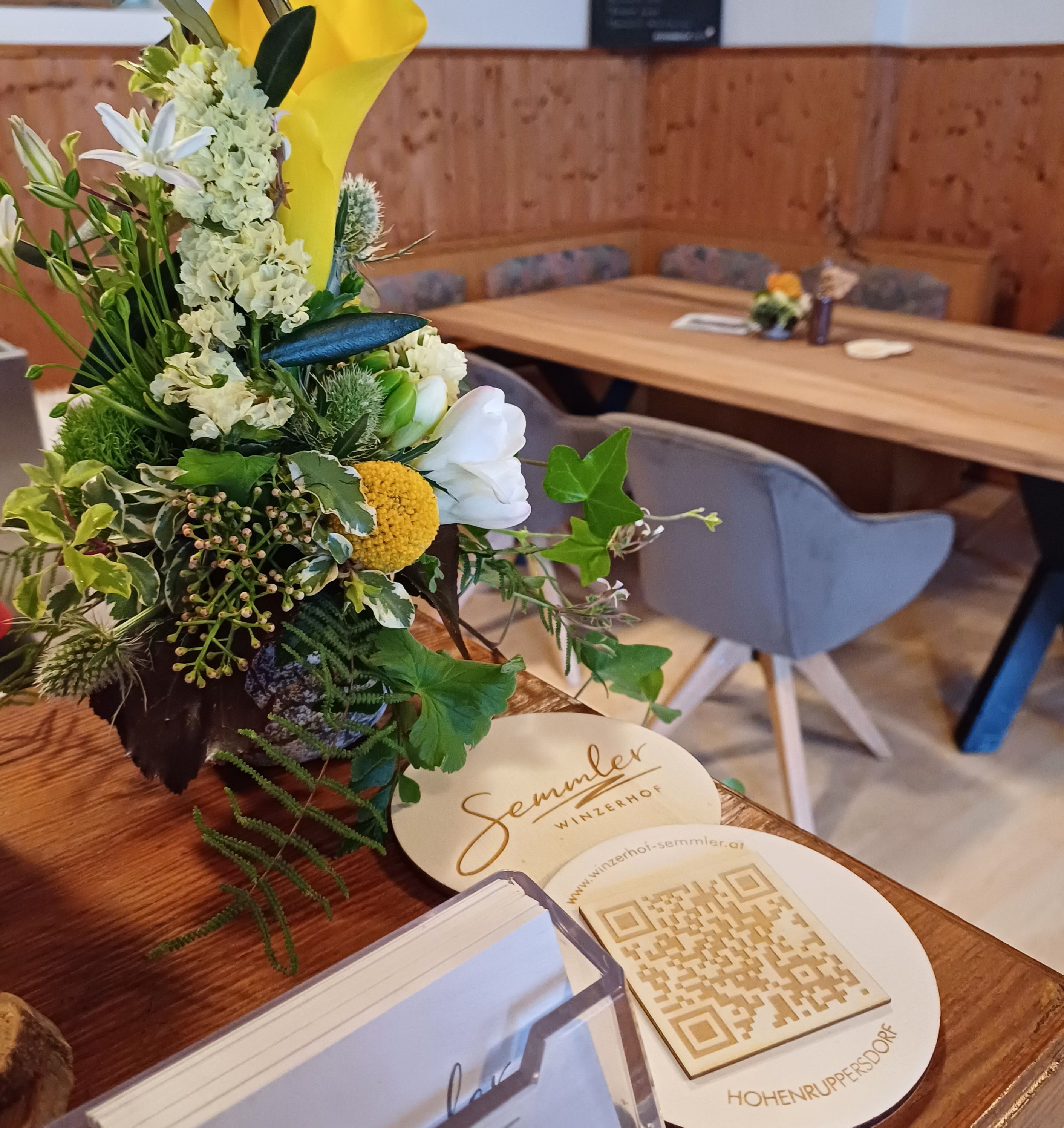 Egy virágcsokor a Winzerhof Semmler egyik asztalán QR-kóddal és névjegykártyákkal.